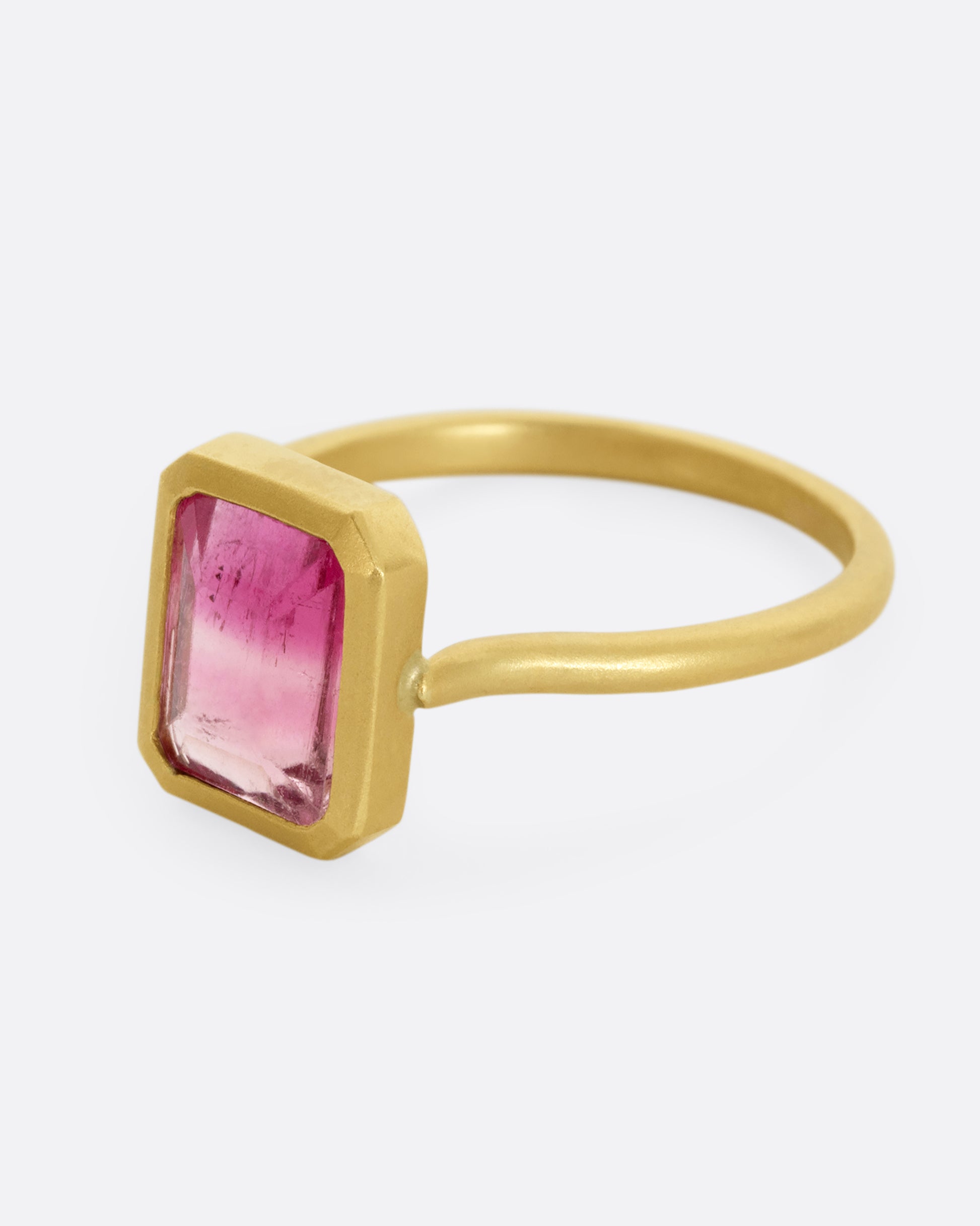 A yellow gold ring with a bezel set rectangular pink bicolor tourmaline. Shown from the side.