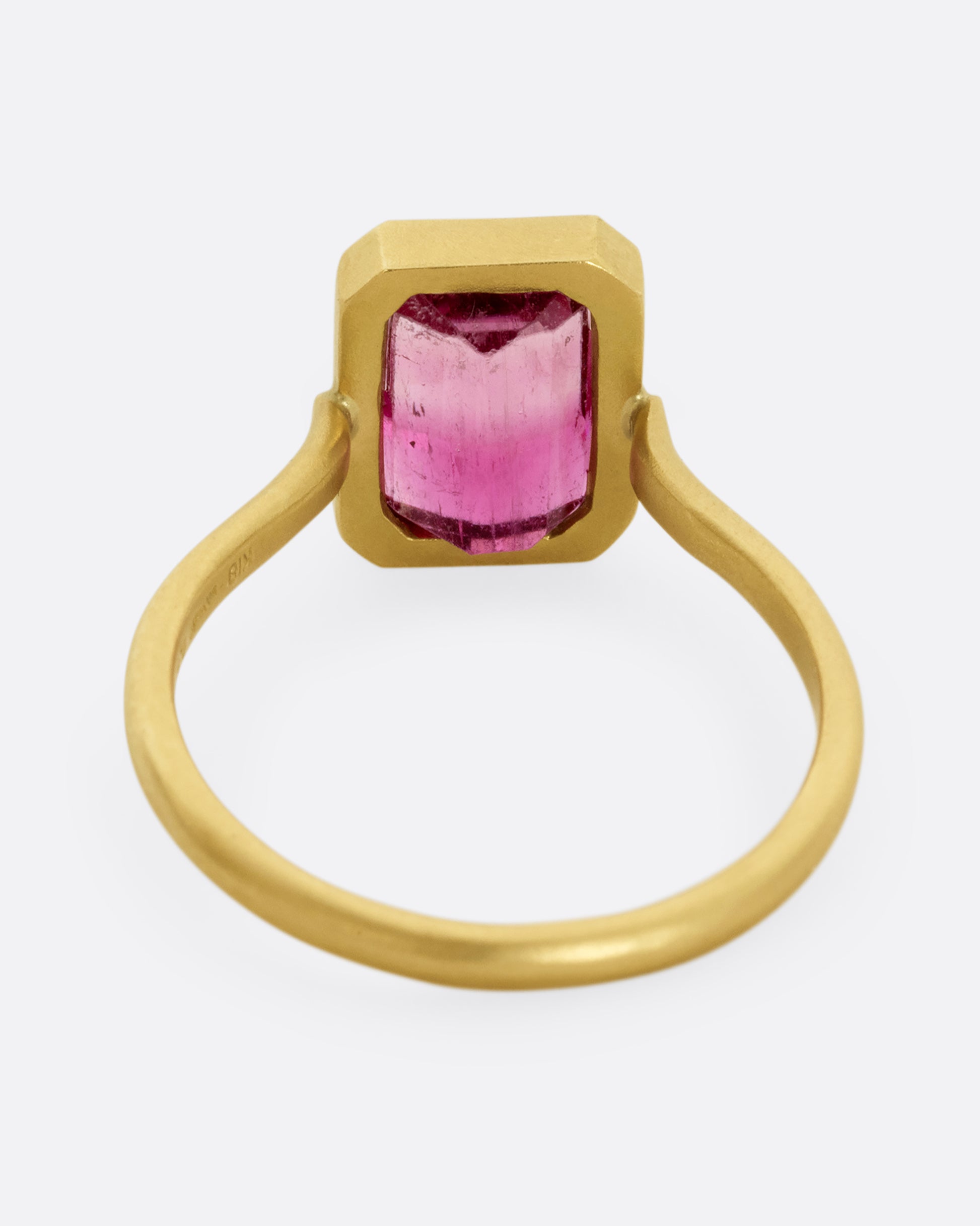 A yellow gold ring with a bezel set rectangular pink bicolor tourmaline. Shown from the back.