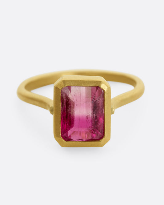 A yellow gold ring with a bezel set rectangular pink bicolor tourmaline. Shown from the front.