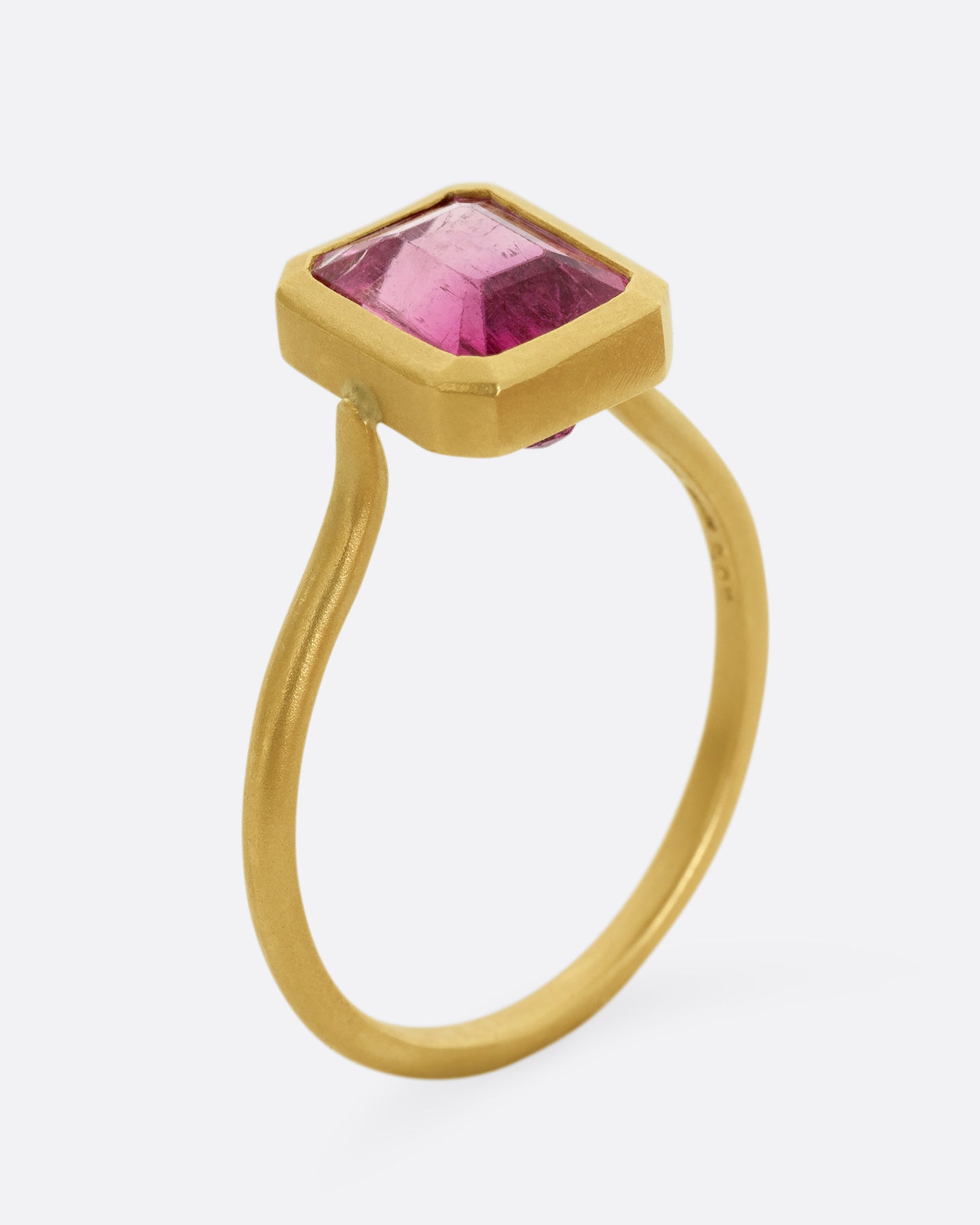 A yellow gold ring with a bezel set rectangular pink bicolor tourmaline. Shown standing up from the side.
