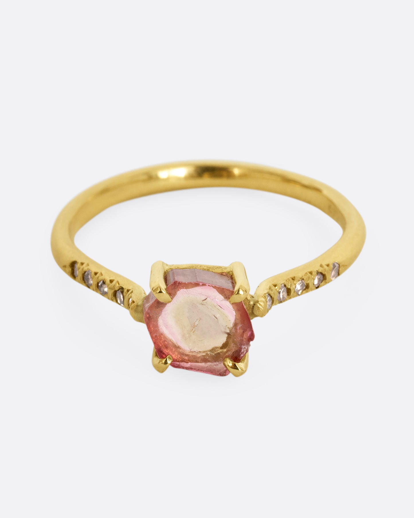 A yellow gold ring with a prong set pale pink bicolor tourmaline and four diamonds on either side of the band. Shown from the front.