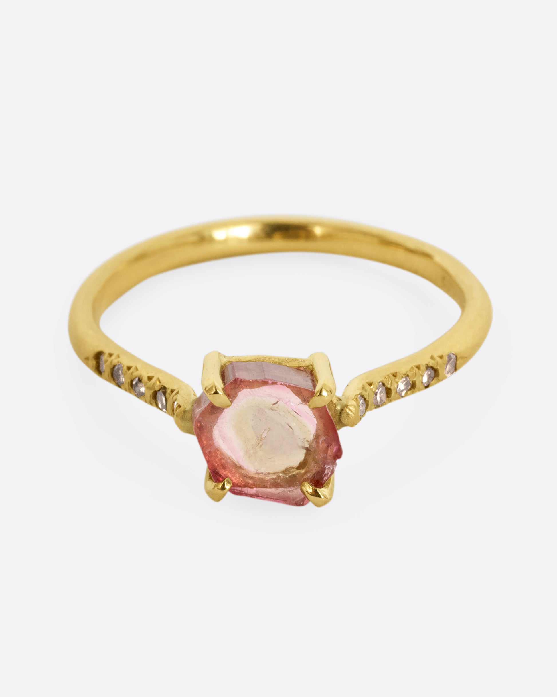 A yellow gold ring with a prong set pale pink bicolor tourmaline and four diamonds on either side of the band. Shown from the front.