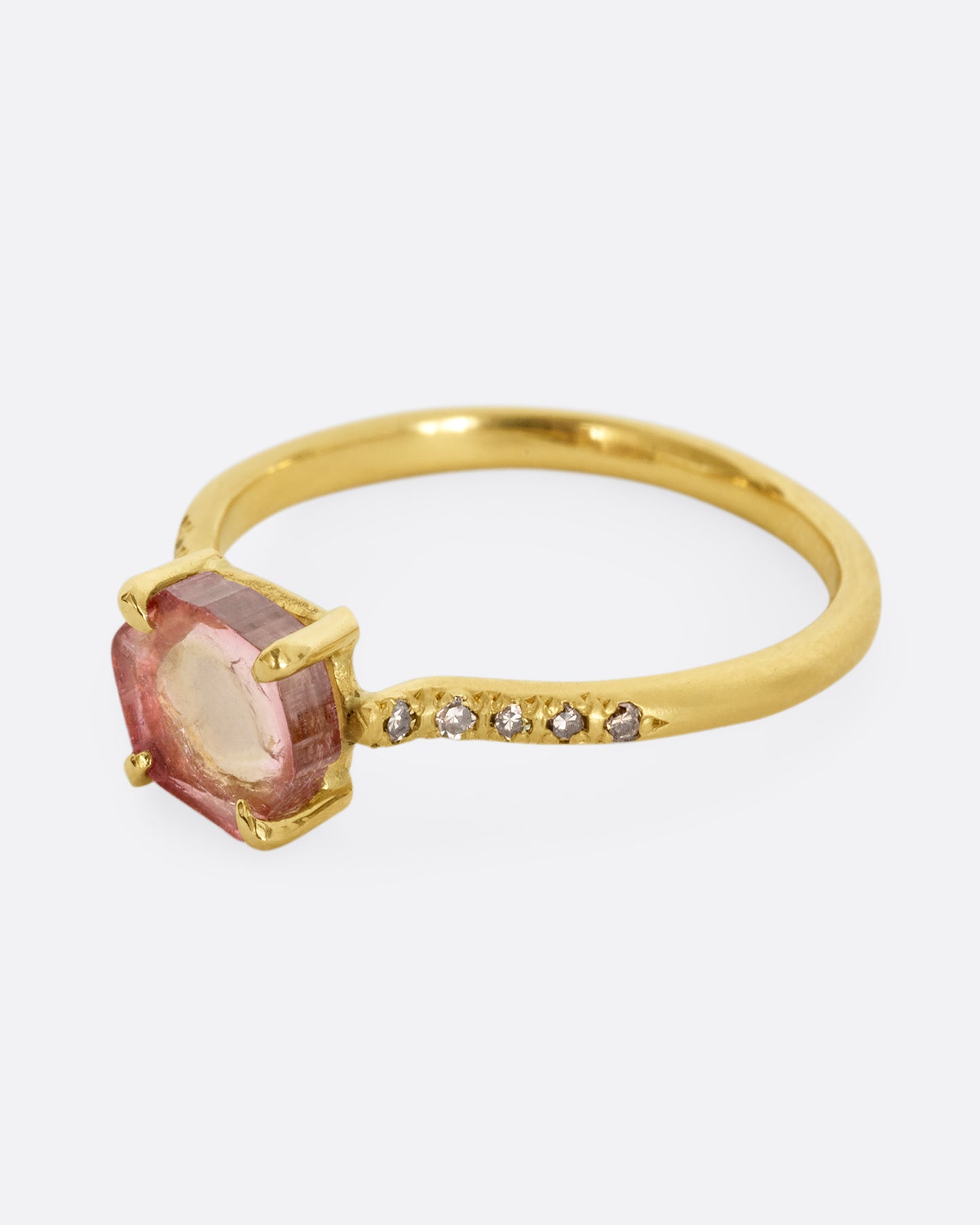 A yellow gold ring with a prong set pale pink bicolor tourmaline and four diamonds on either side of the band. Shown from the side.
