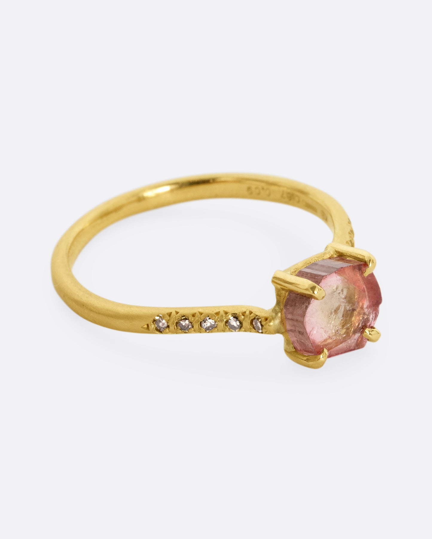 A yellow gold ring with a prong set pale pink bicolor tourmaline and four diamonds on either side of the band. Shown from the side.