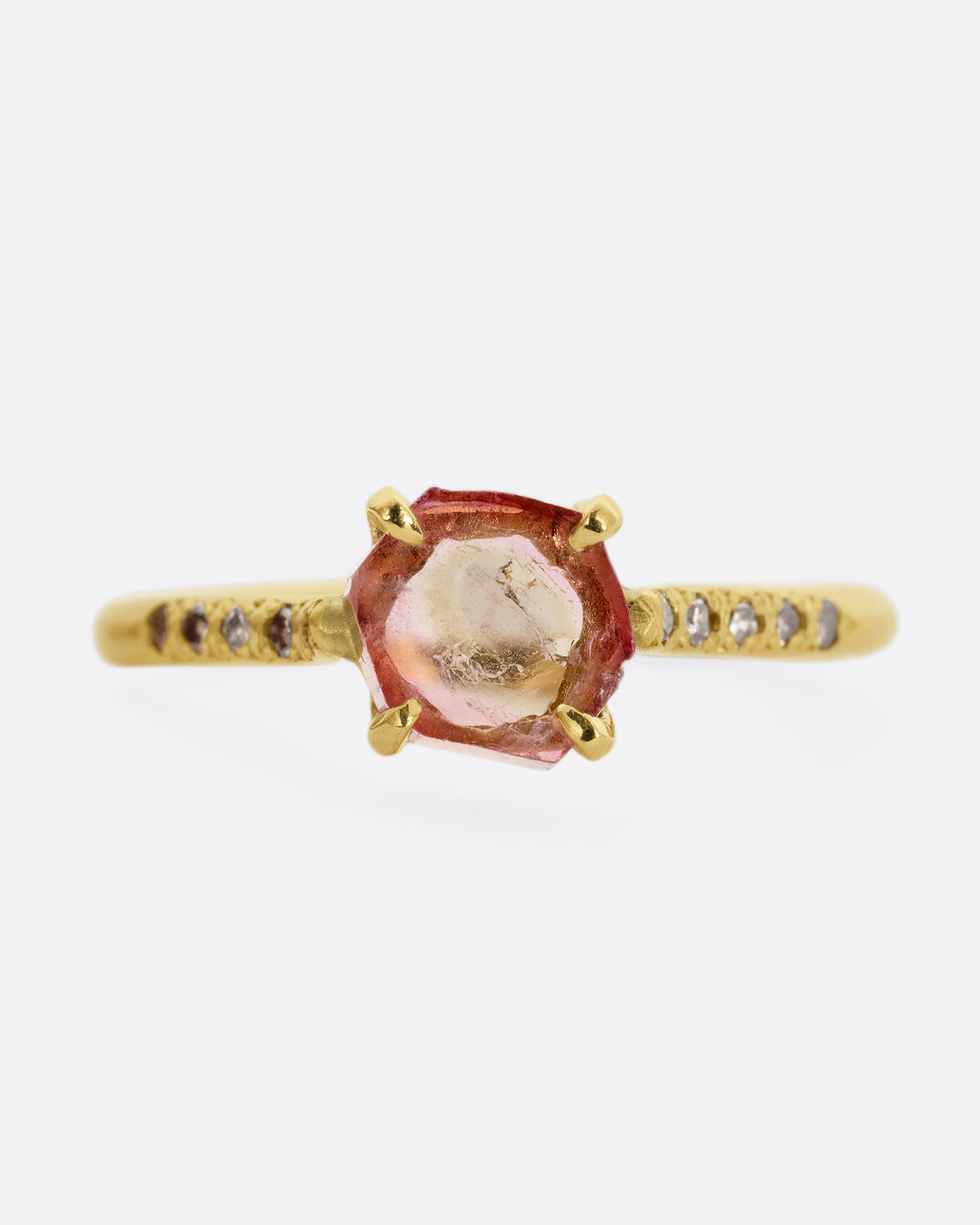 A yellow gold ring with a prong set pale pink bicolor tourmaline and four diamonds on either side of the band. Shown from the front.