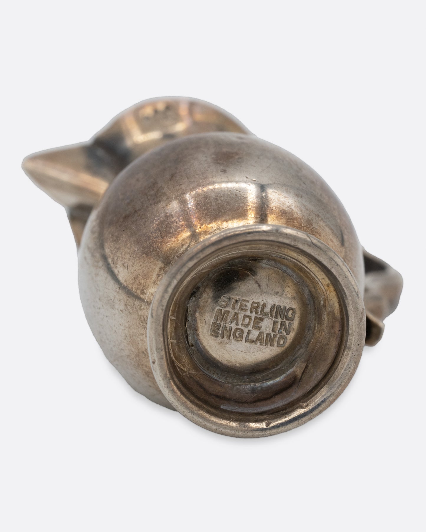 A tiny silver pitcher with an engraved flower, a spout, and handle. Shown from the bottom.