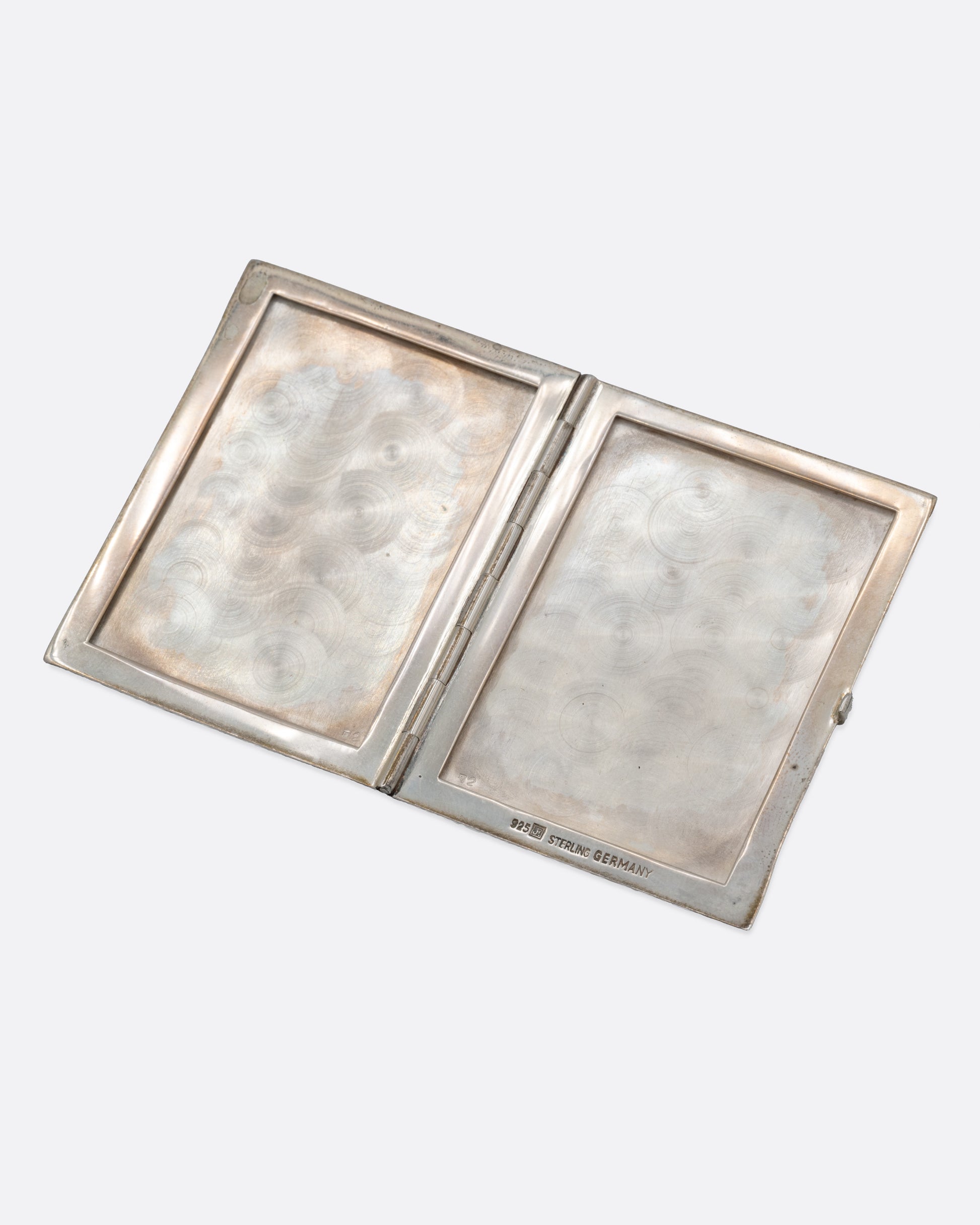 A silver picture frame with a textured exterior and two spots for photos, shown open.