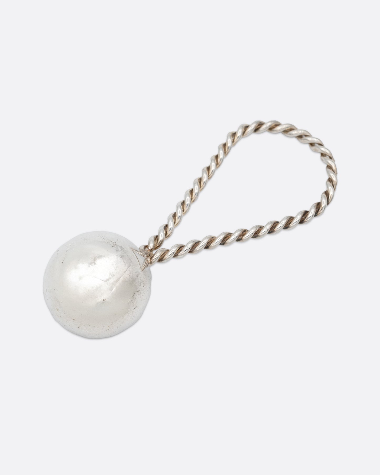 A silver rattle with a sphere at one and a twisted loop at the other. Shown from the front.