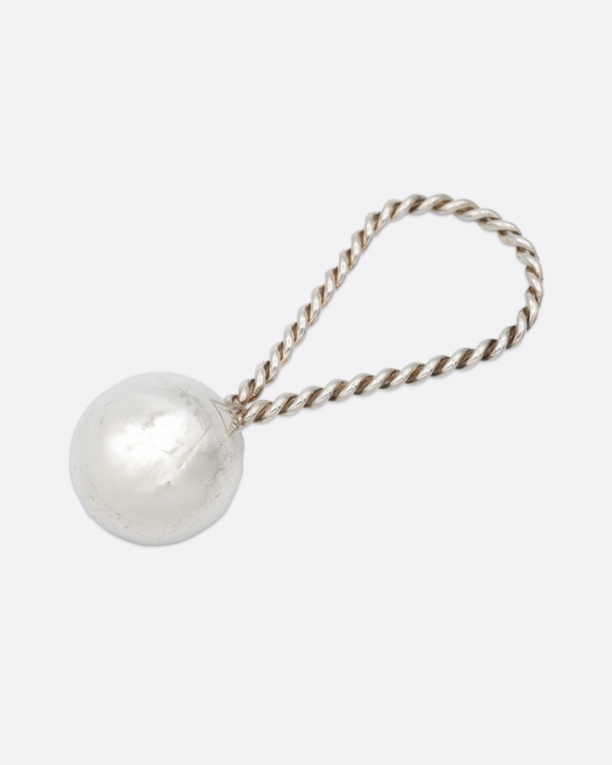 A silver rattle with a sphere at one and a twisted loop at the other. Shown from the front.