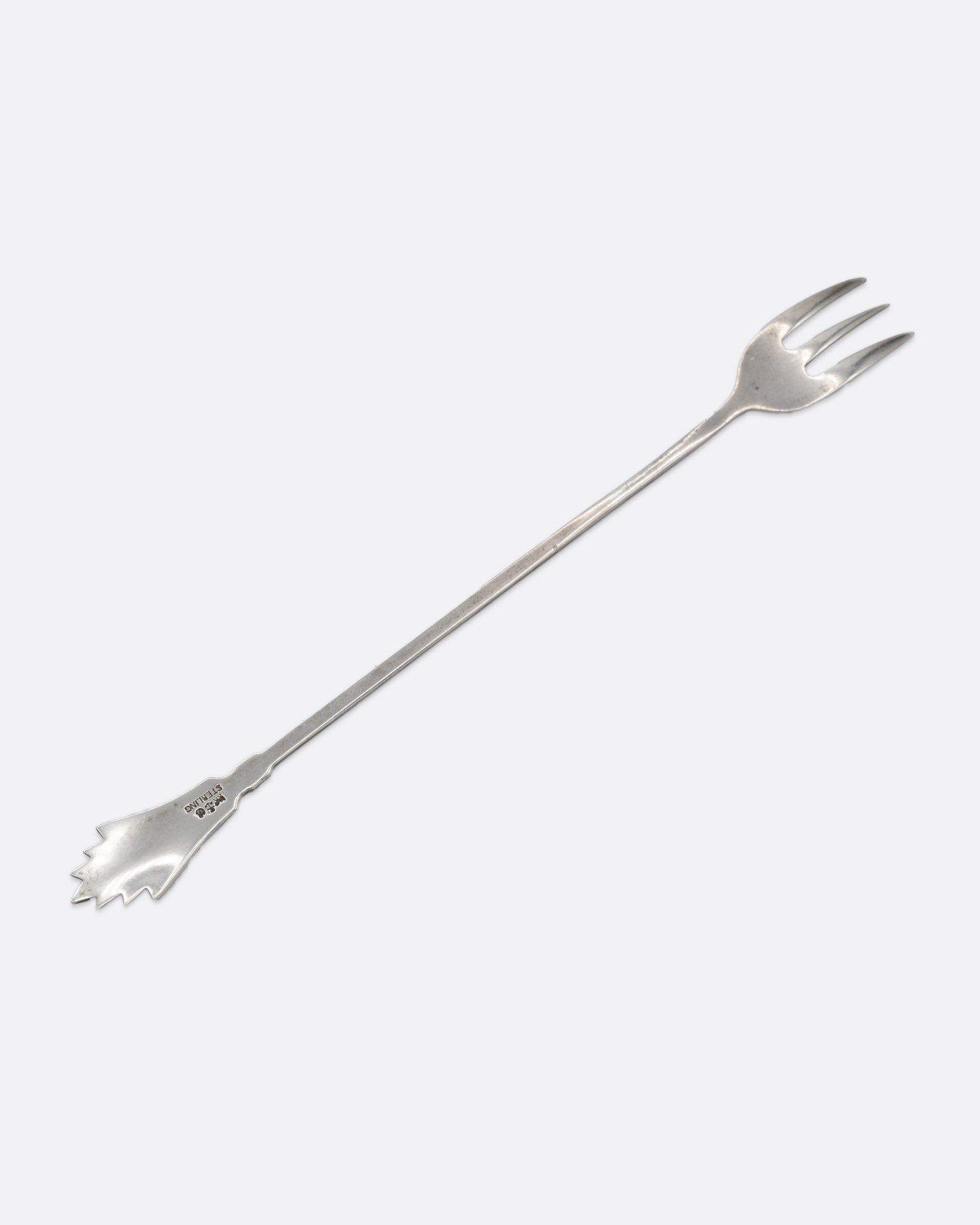 A silver three pronged fork with a fan shape at the top of the handle. Shown from the back.