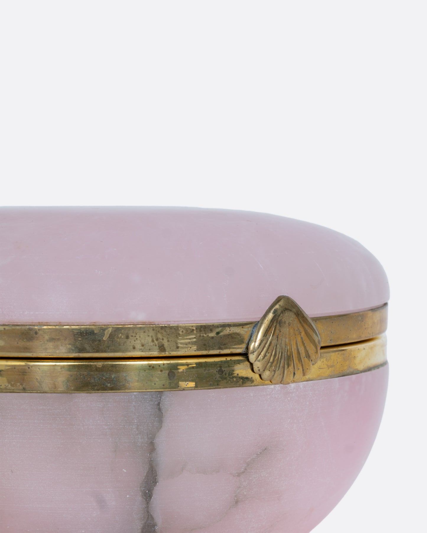 A close up of a round pink alabaster box with gold edges and a seashell shaped clasp.
