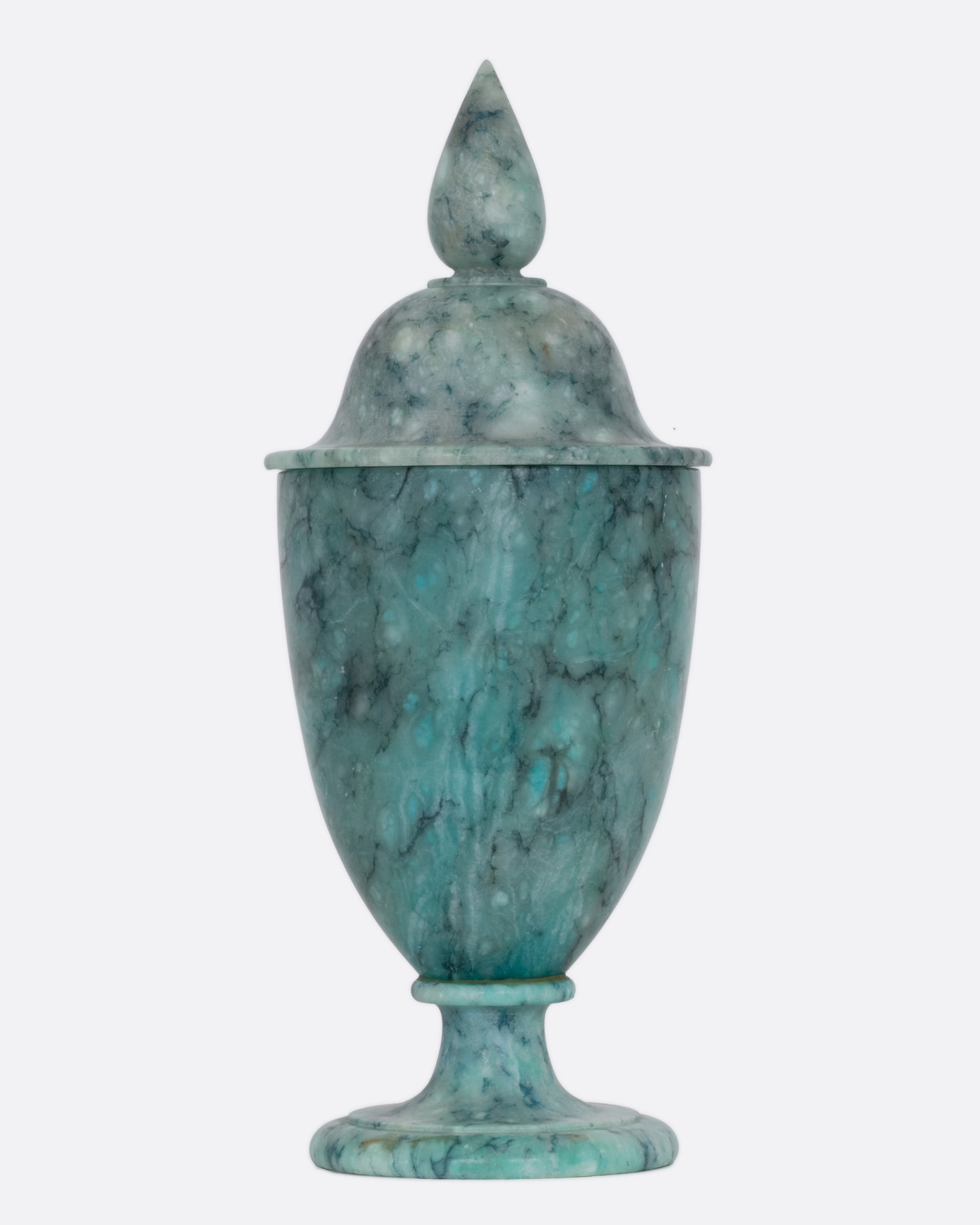 A turquoise colored ornate alabaster vessel with a lid, shown from the front.