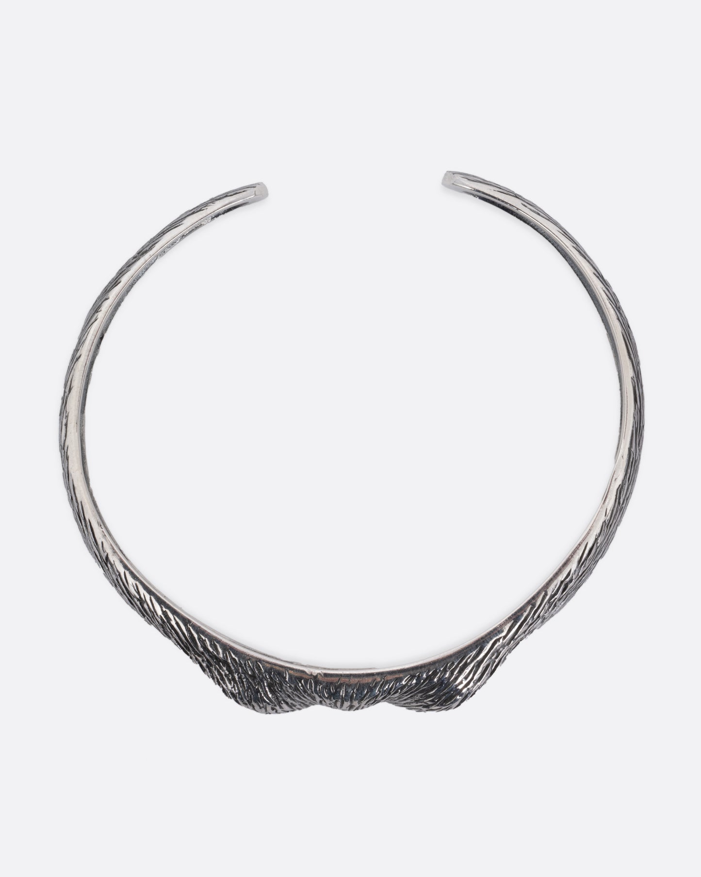 A silver bracelet with blue glass eyes and an all-over carved texture. Shown from the top.