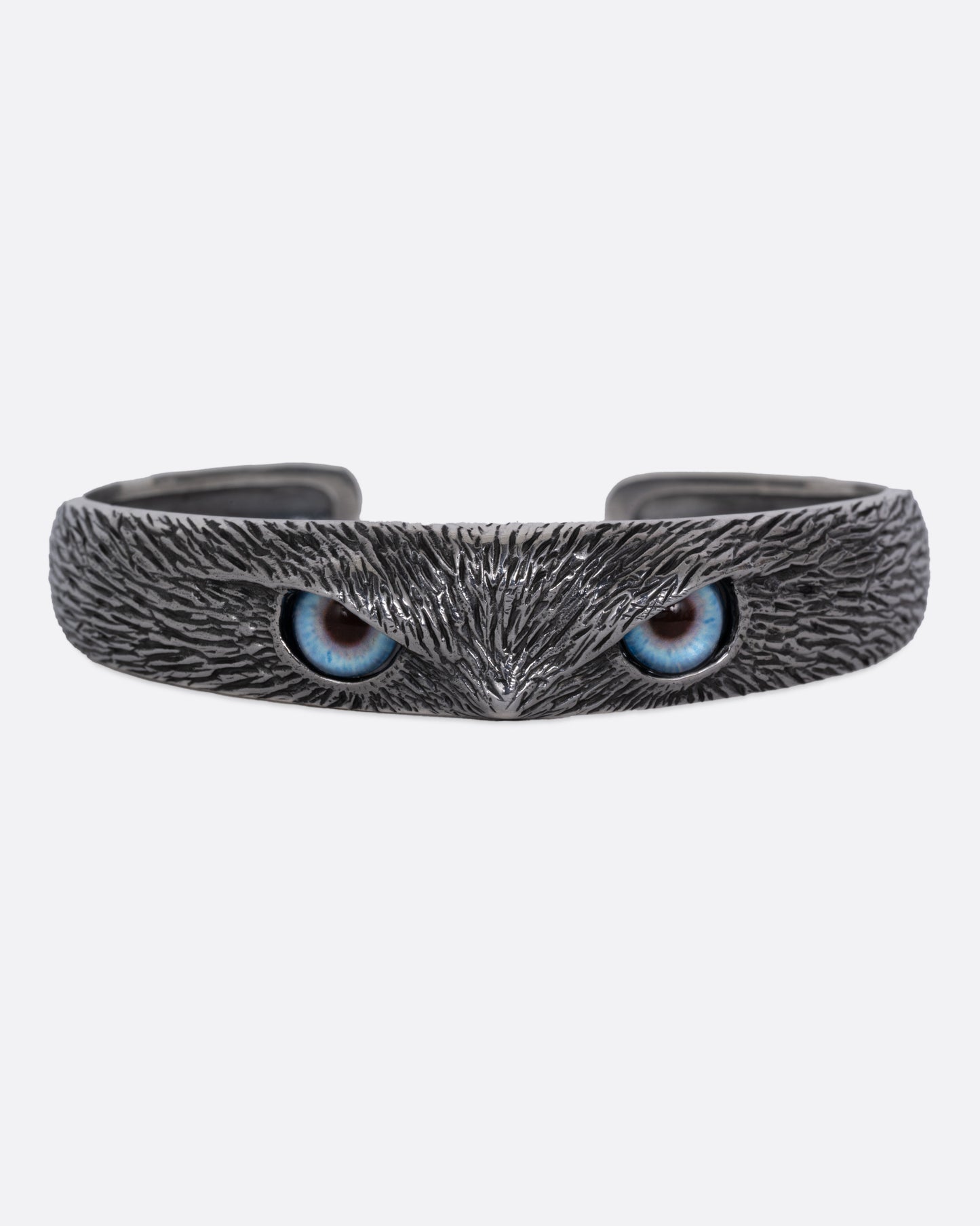 A silver bracelet with blue glass eyes and an all-over carved texture. Shown from the front.