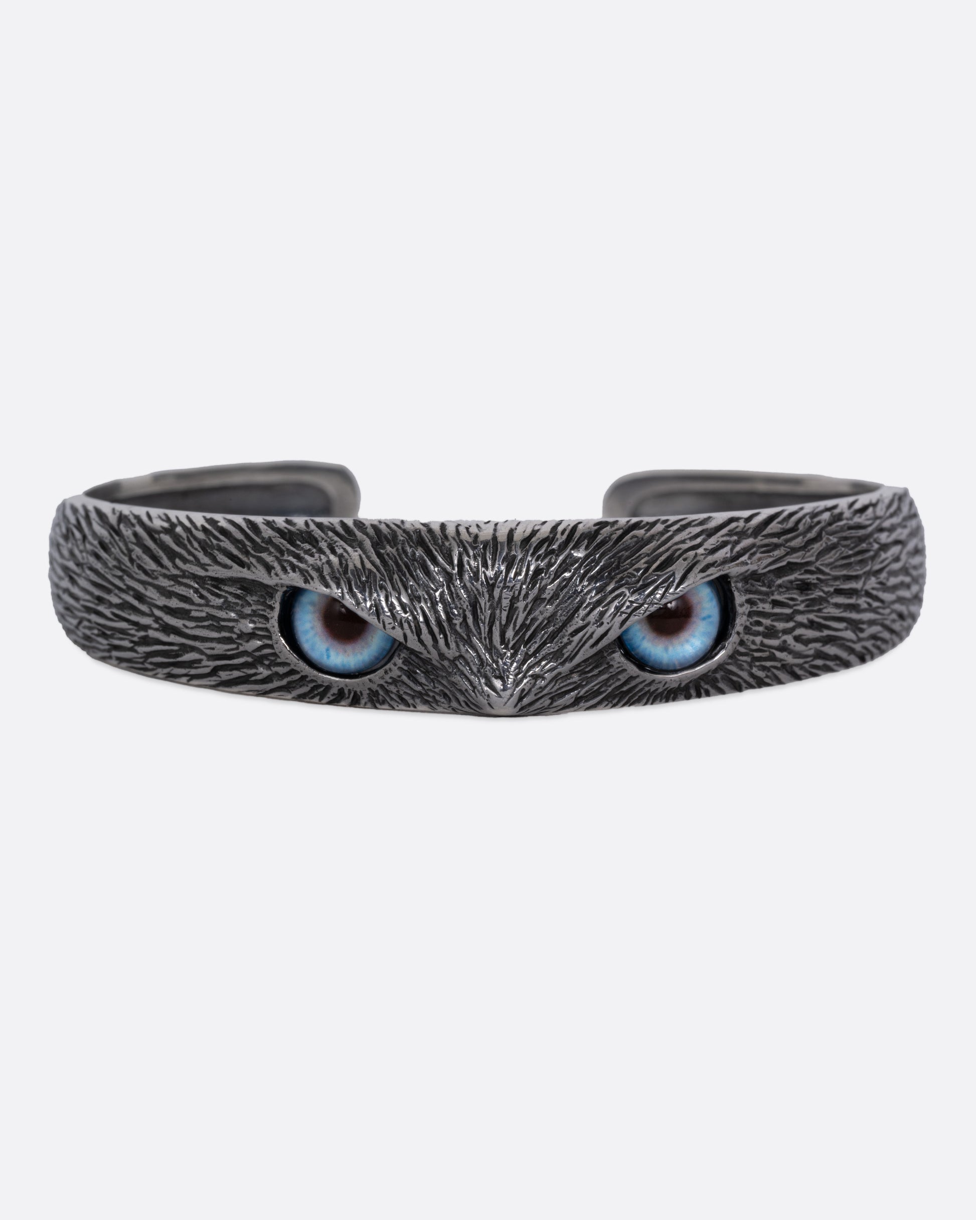 A silver bracelet with blue glass eyes and an all-over carved texture. Shown from the front.
