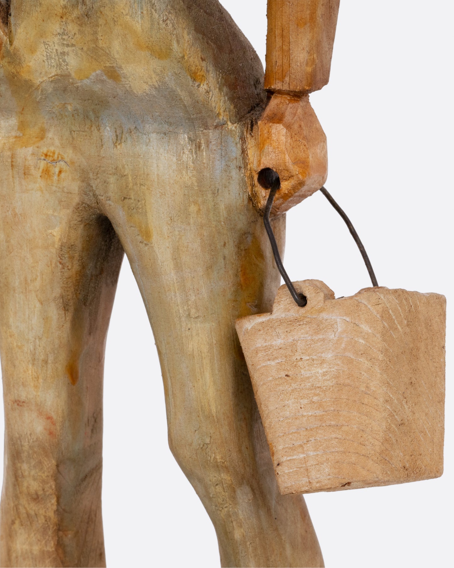 A close up of a wooden hand carved and painted folk art cowgirl holding a bucket. 