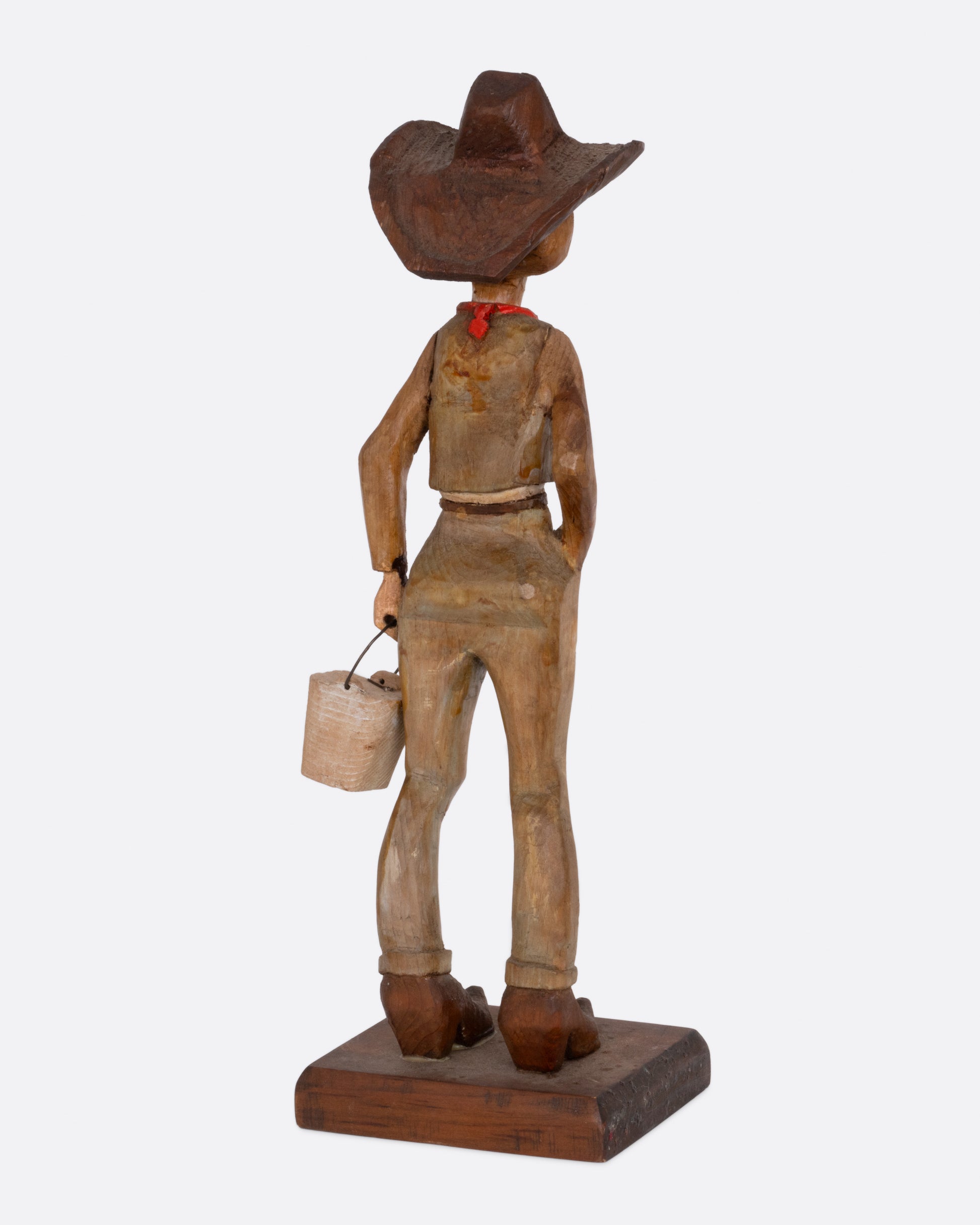  A wooden hand carved and painted folk art cowgirl holding a bucket. Shown from the back.