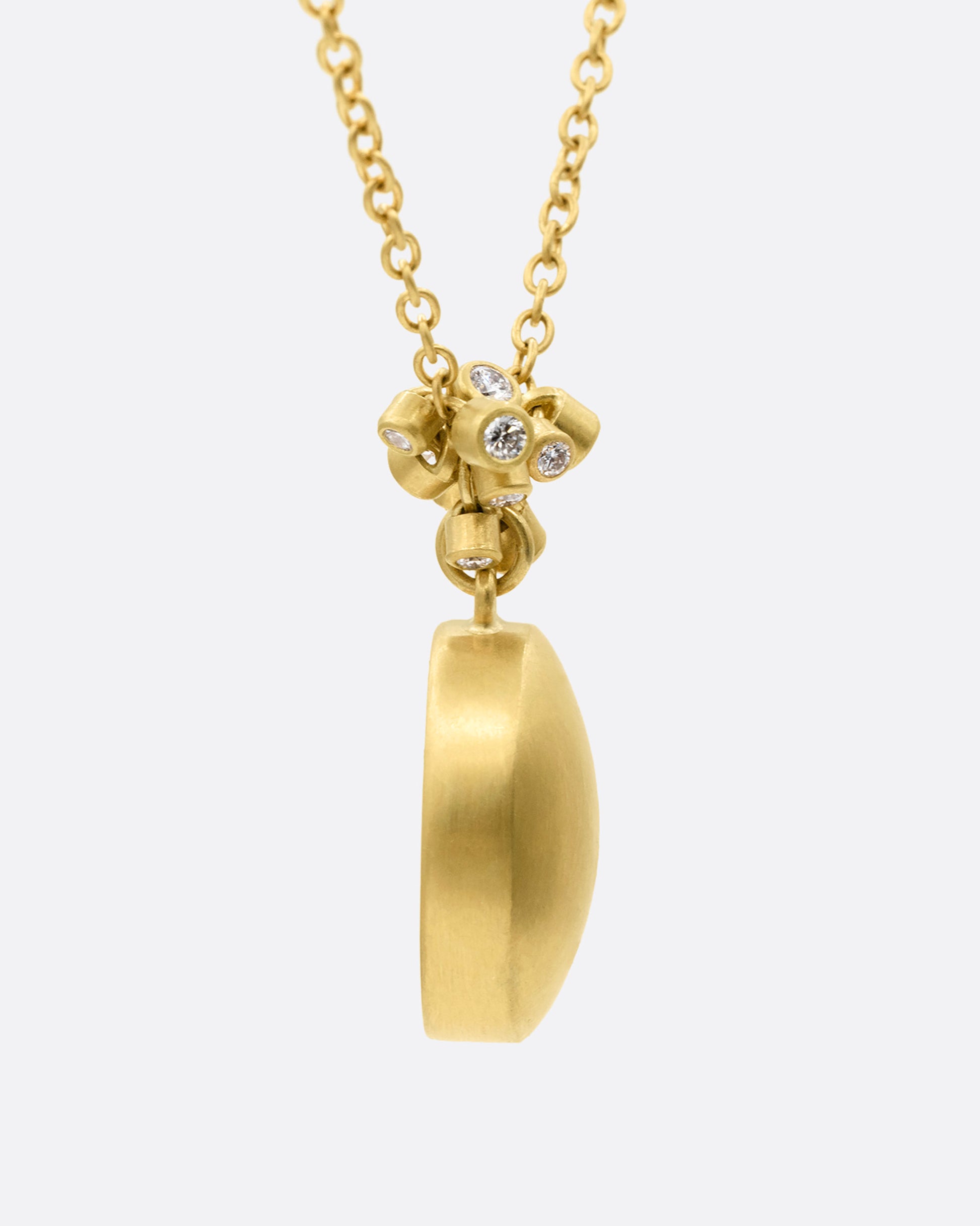A yellow gold pendant necklace with a amethyst with a hand carved strawberry and a cluster of diamond charms, shown from the side.