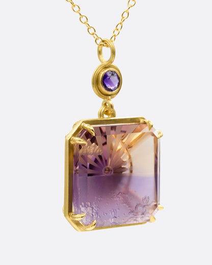 A yellow gold pendant necklace with an ametrine sunset carving with a gold sun face on its reverse. A round amethyst hovers just above this double sided pendant. Shown from the side.