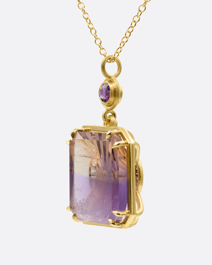 A yellow gold pendant necklace with an ametrine sunset carving with a gold sun face on its reverse. A round amethyst hovers just above this double sided pendant. Shown from the side.