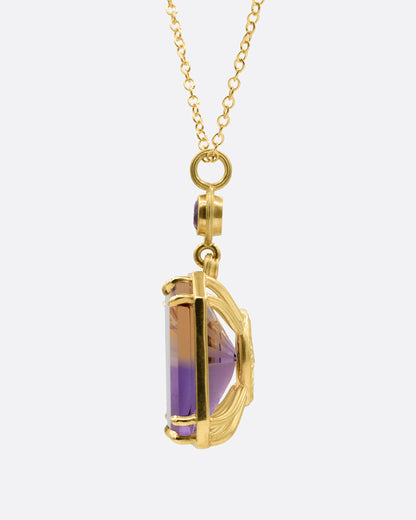 A yellow gold pendant necklace with an ametrine sunset carving with a gold sun face on its reverse. A round amethyst hovers just above this double sided pendant. Shown from the side.
