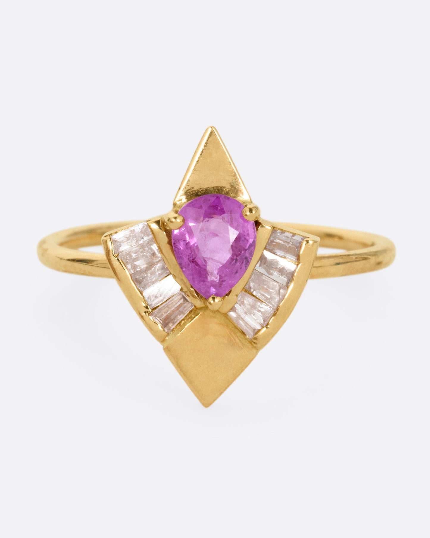 A yellow gold ring with a pink sapphire and baguette diamonds, shown from the front.