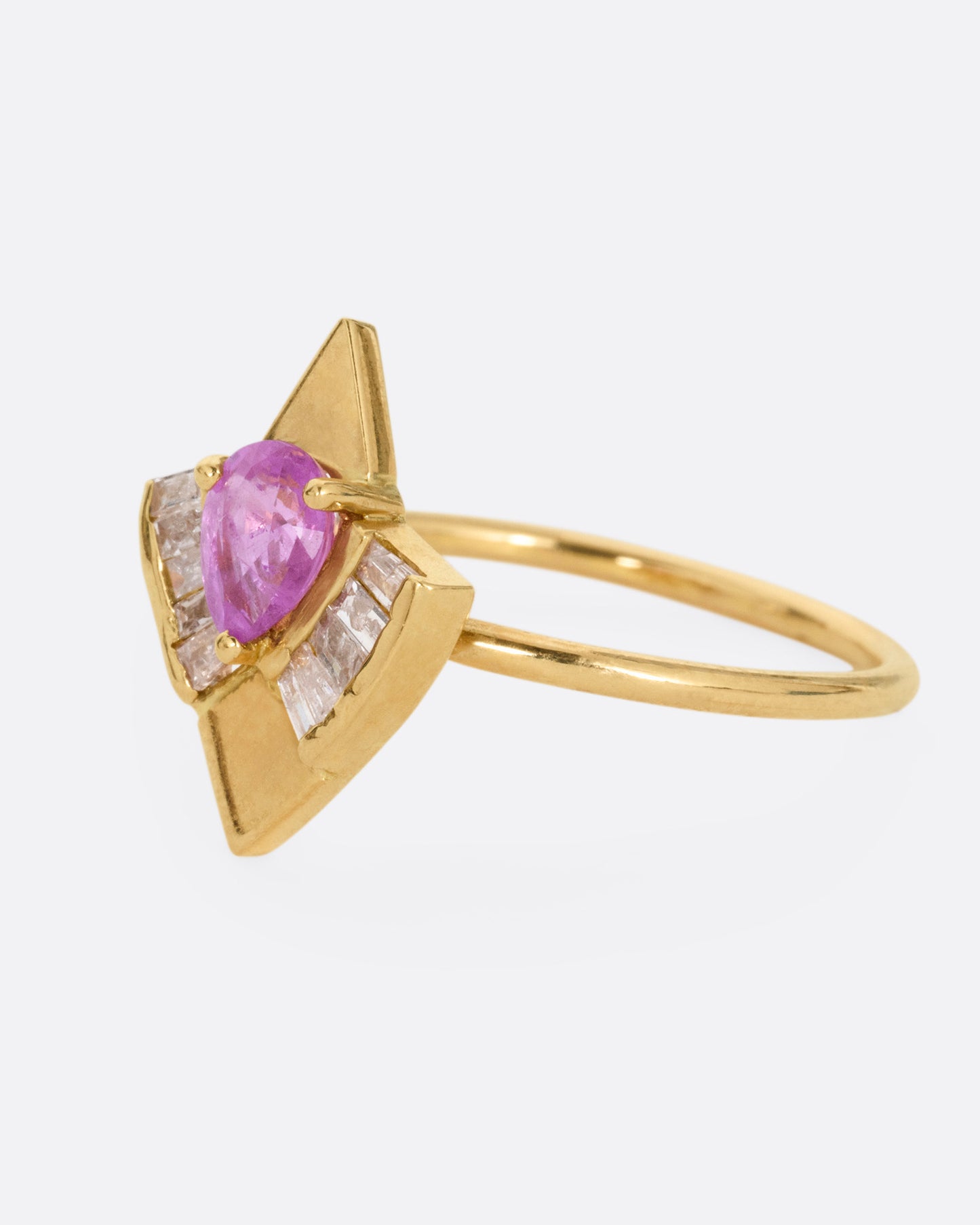 A yellow gold ring with a pink sapphire and baguette diamonds, shown from the side.