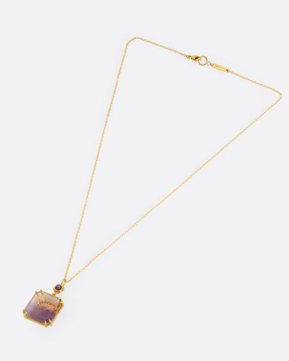 A yellow gold pendant necklace with an ametrine sunset carving with a gold sun face on its reverse. A round amethyst hovers just above this double sided pendant. Shown from the front.