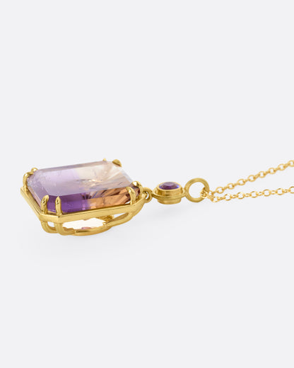 A yellow gold pendant necklace with an ametrine sunset carving with a gold sun face on its reverse. A round amethyst hovers just above this double sided pendant. Shown from the side.