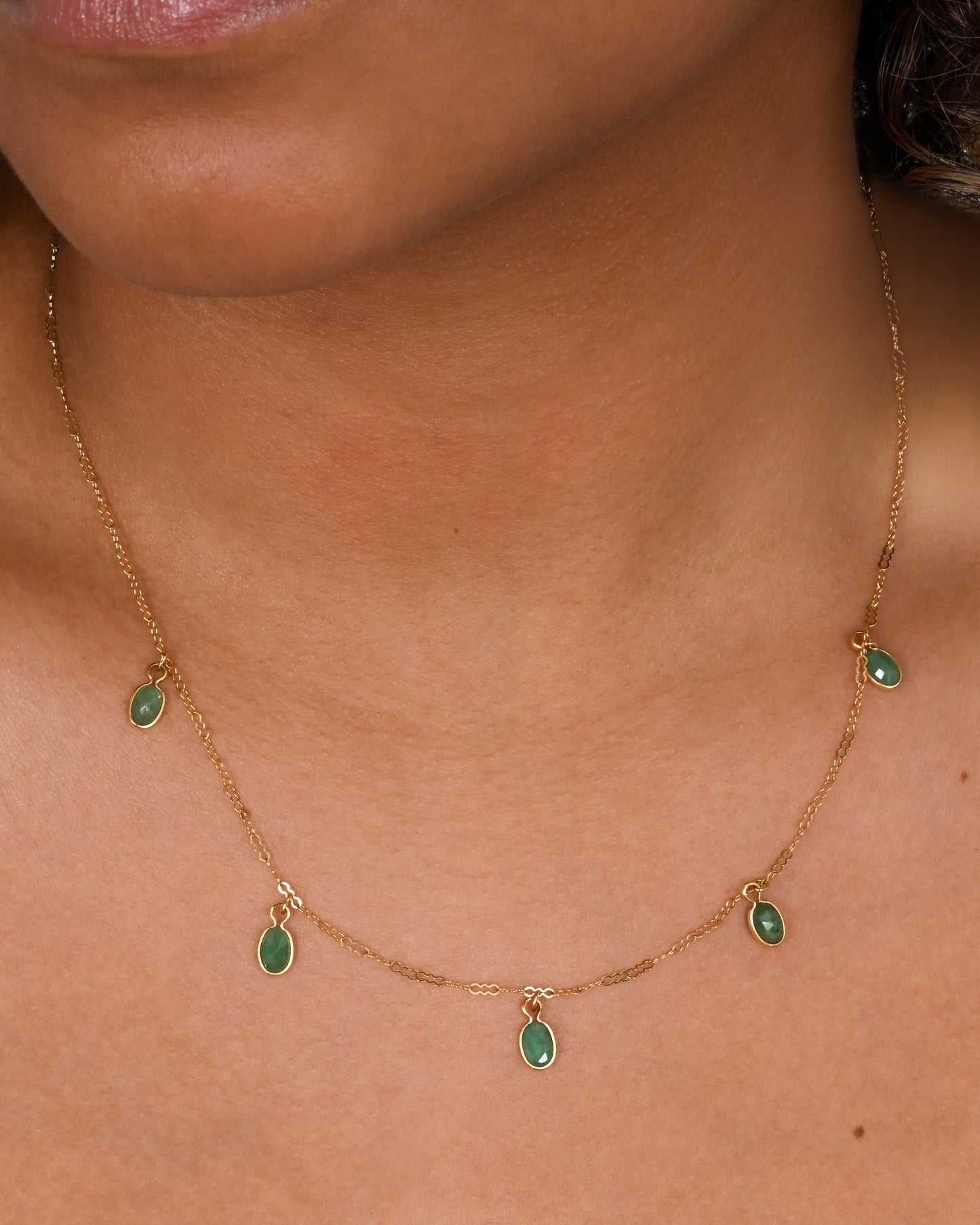 A yellow gold necklace with five oval emeralds. Shown on a neck.