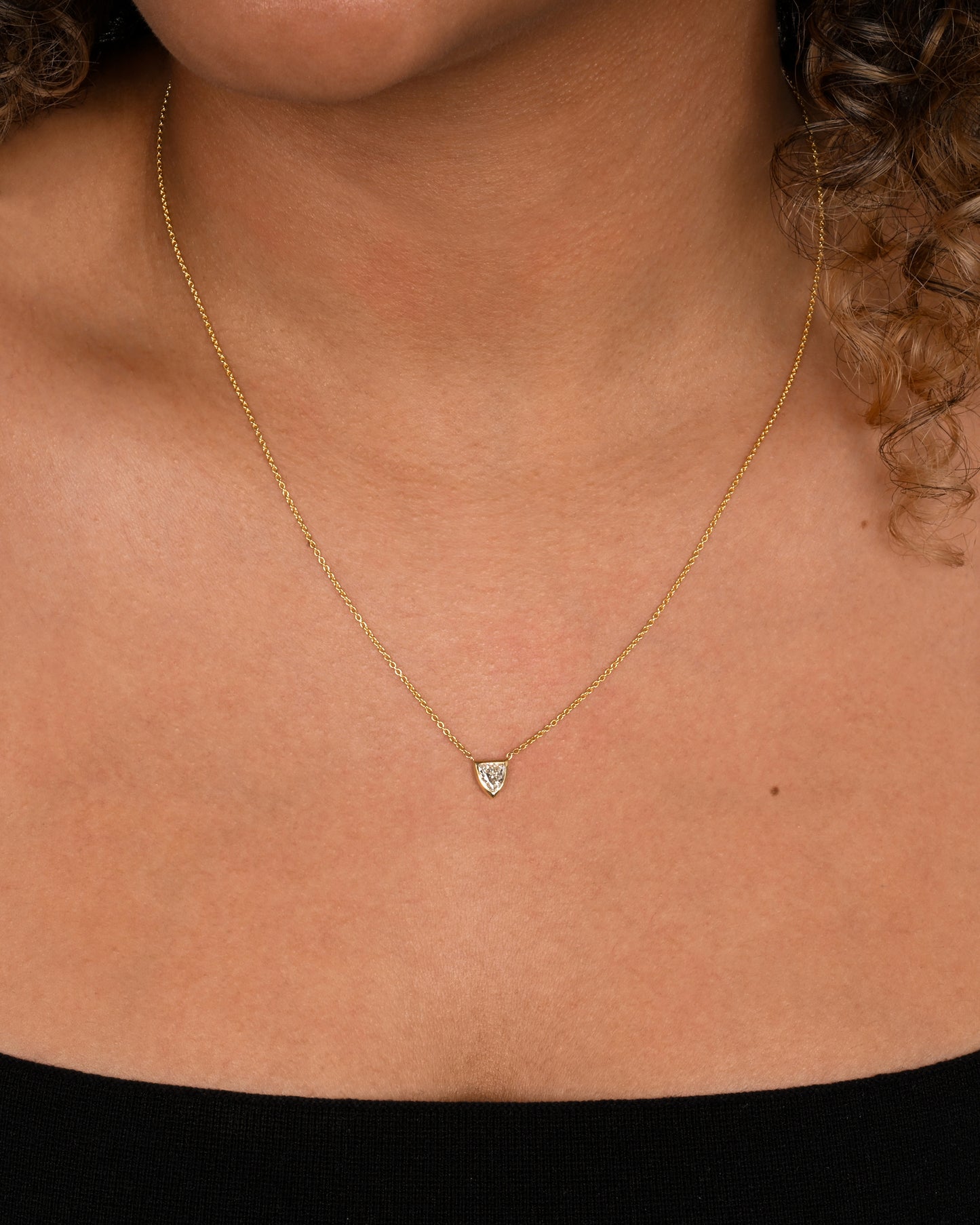 A yellow gold necklace with a shield shaped diamond. Shown worn.