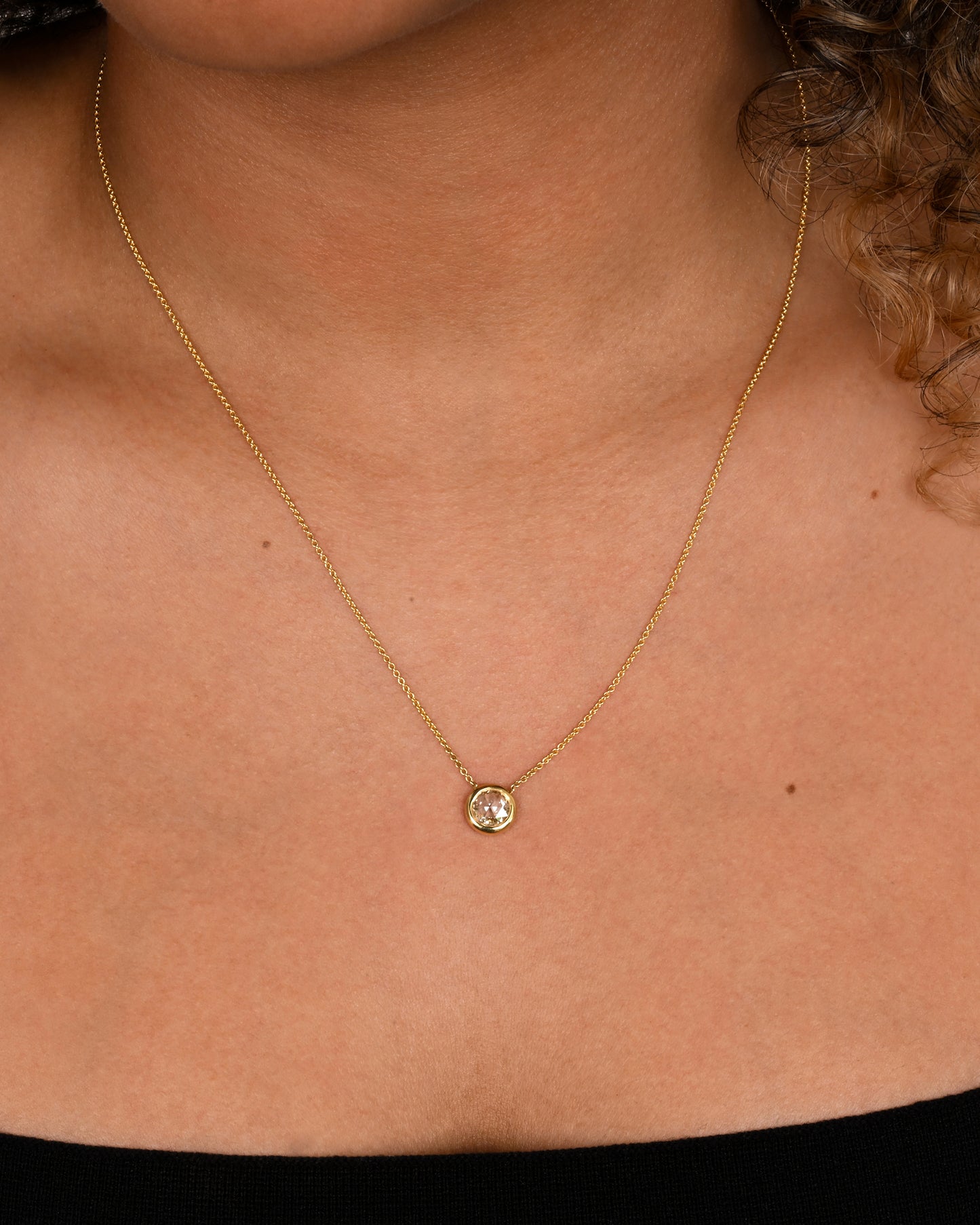 A yellow gold necklace with a circular shaped rose cut diamond. Shown on a neck.