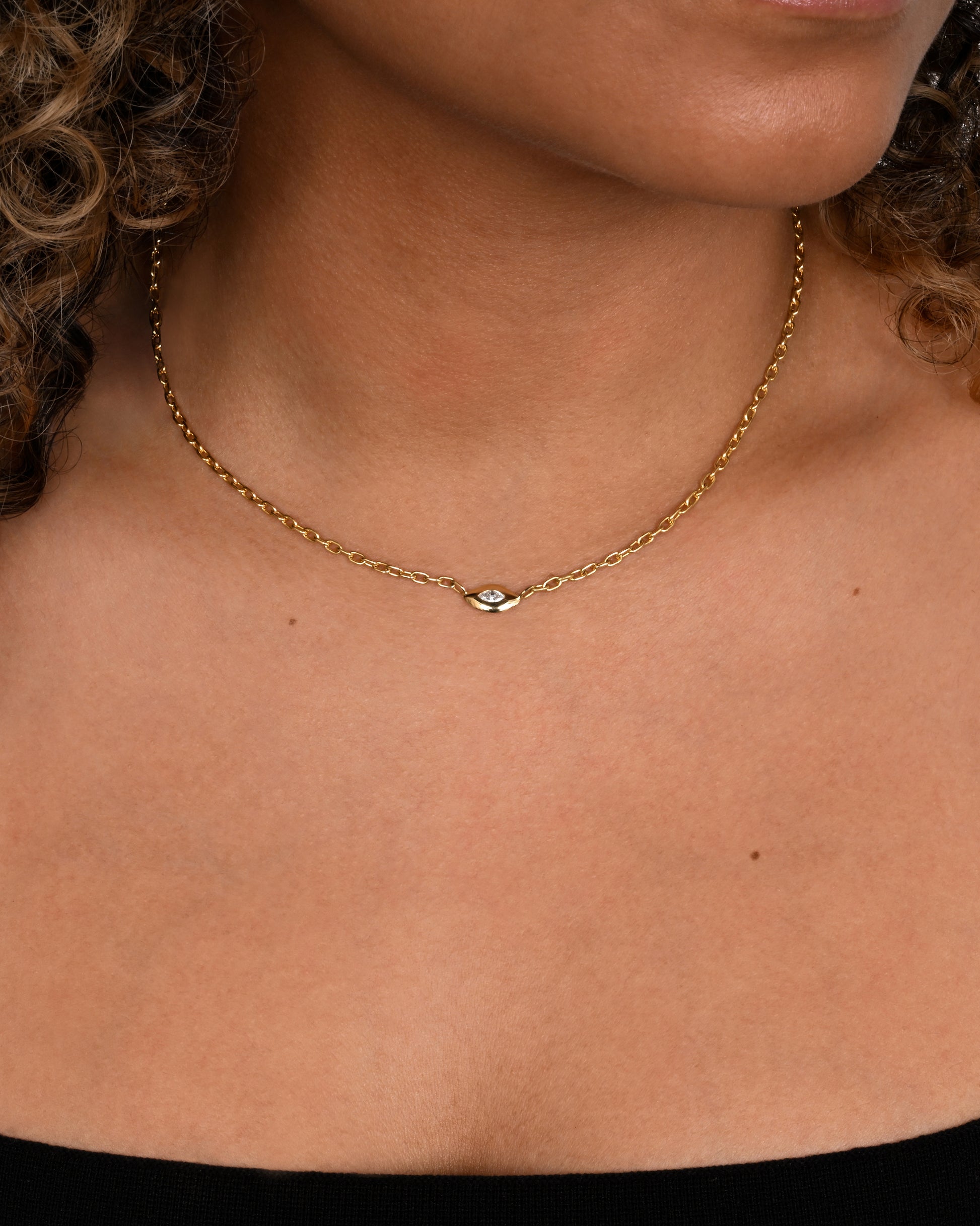 A yellow gold necklace with a marquis diamond pendant. Shown on a neck.