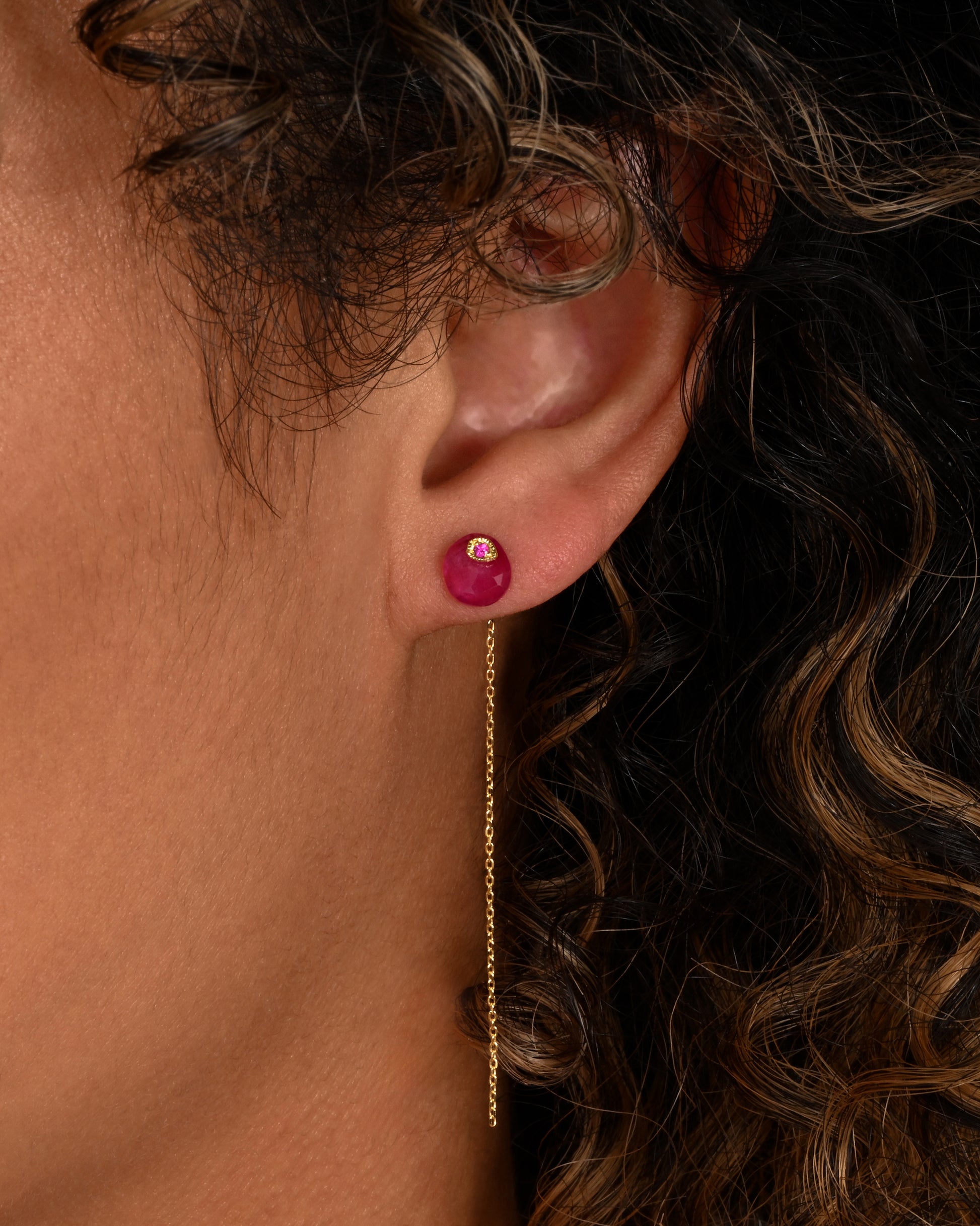 A pin and chain earring with a ruby and cable chain. Shown from the front on a person.