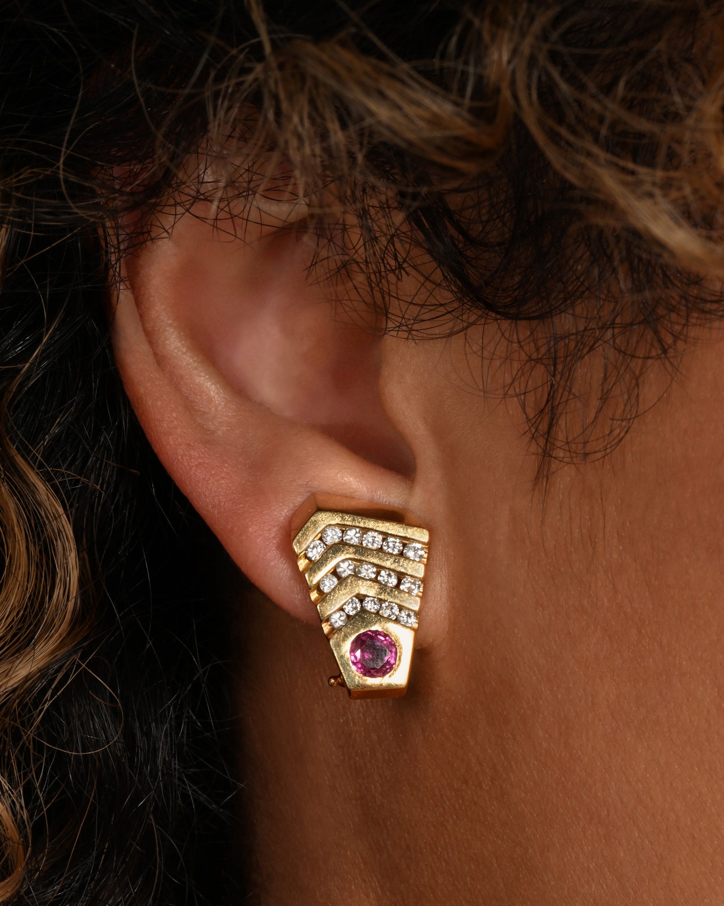 A pair of geometric yellow gold earrings with rubies and diamonds. Shown on an ear.