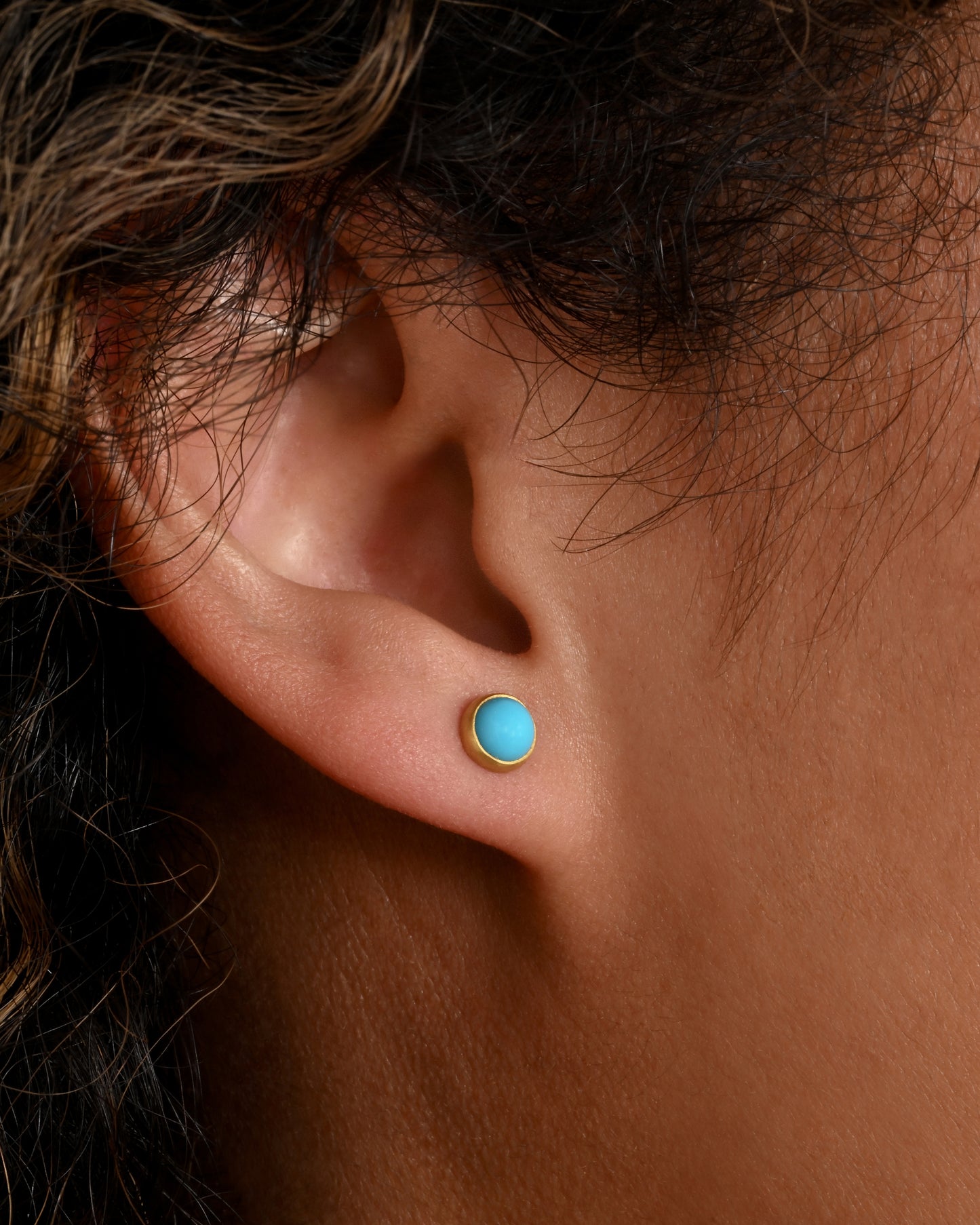 A pair of yellow gold turquoise cabochon stud earrings. Shown on an ear.