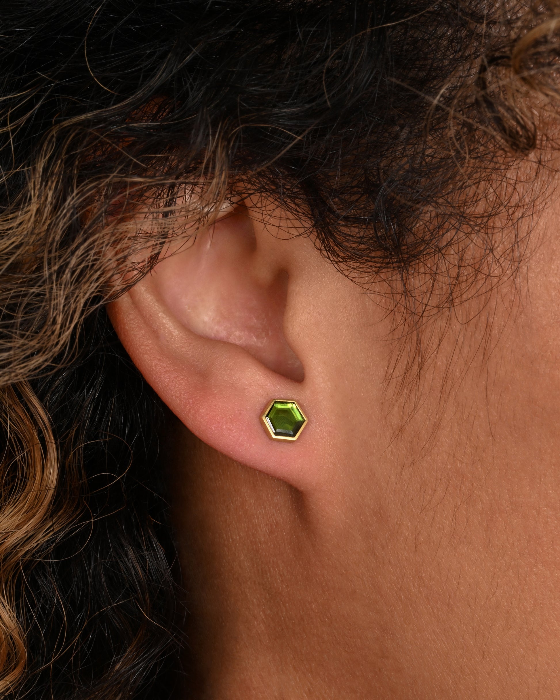 Yellow gold hexagon studs with bezel set green chrome tourmaline. Shown on an ear.