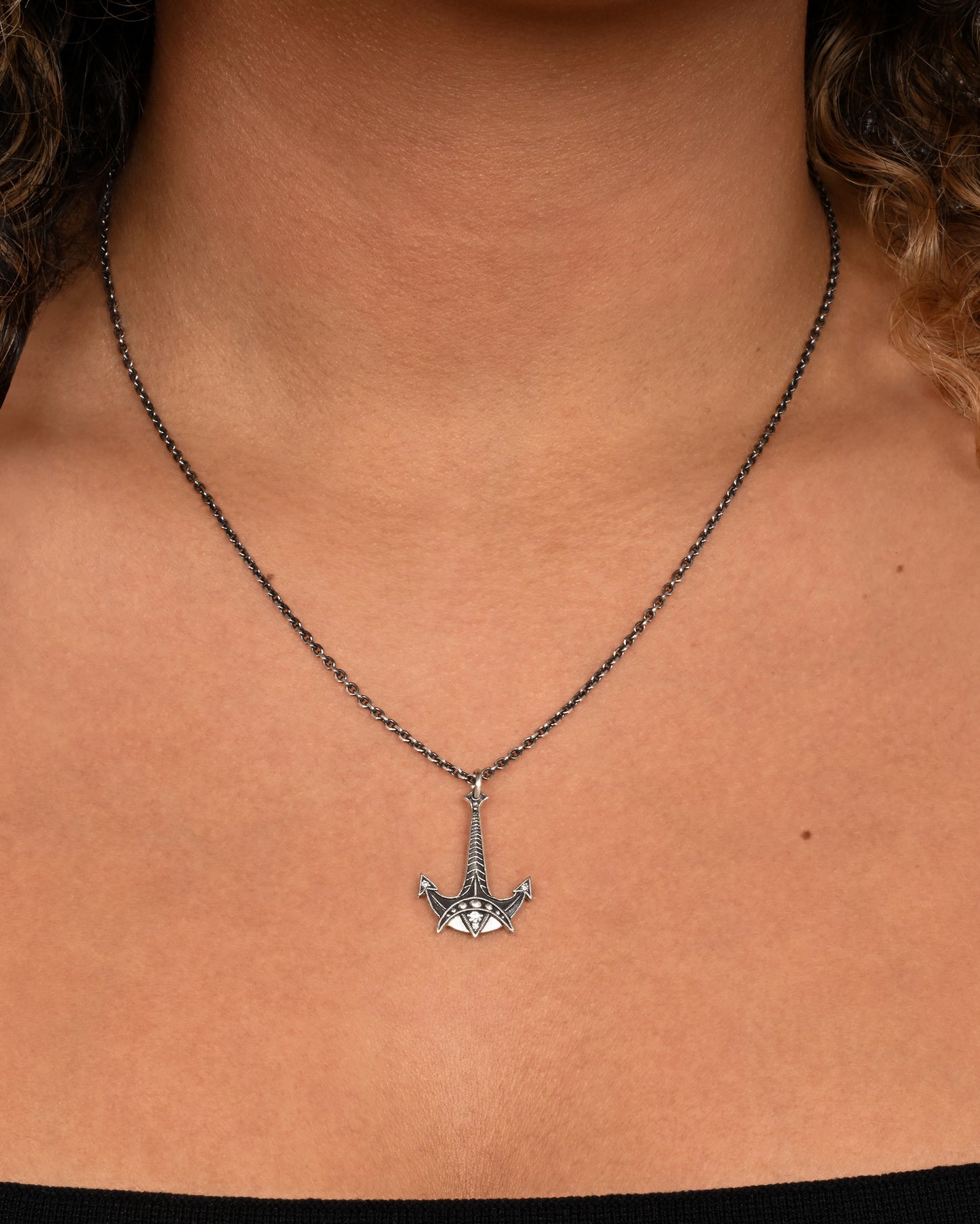 A sterling silver necklace with an anchor pendant and diamond details. Shown on a neck.