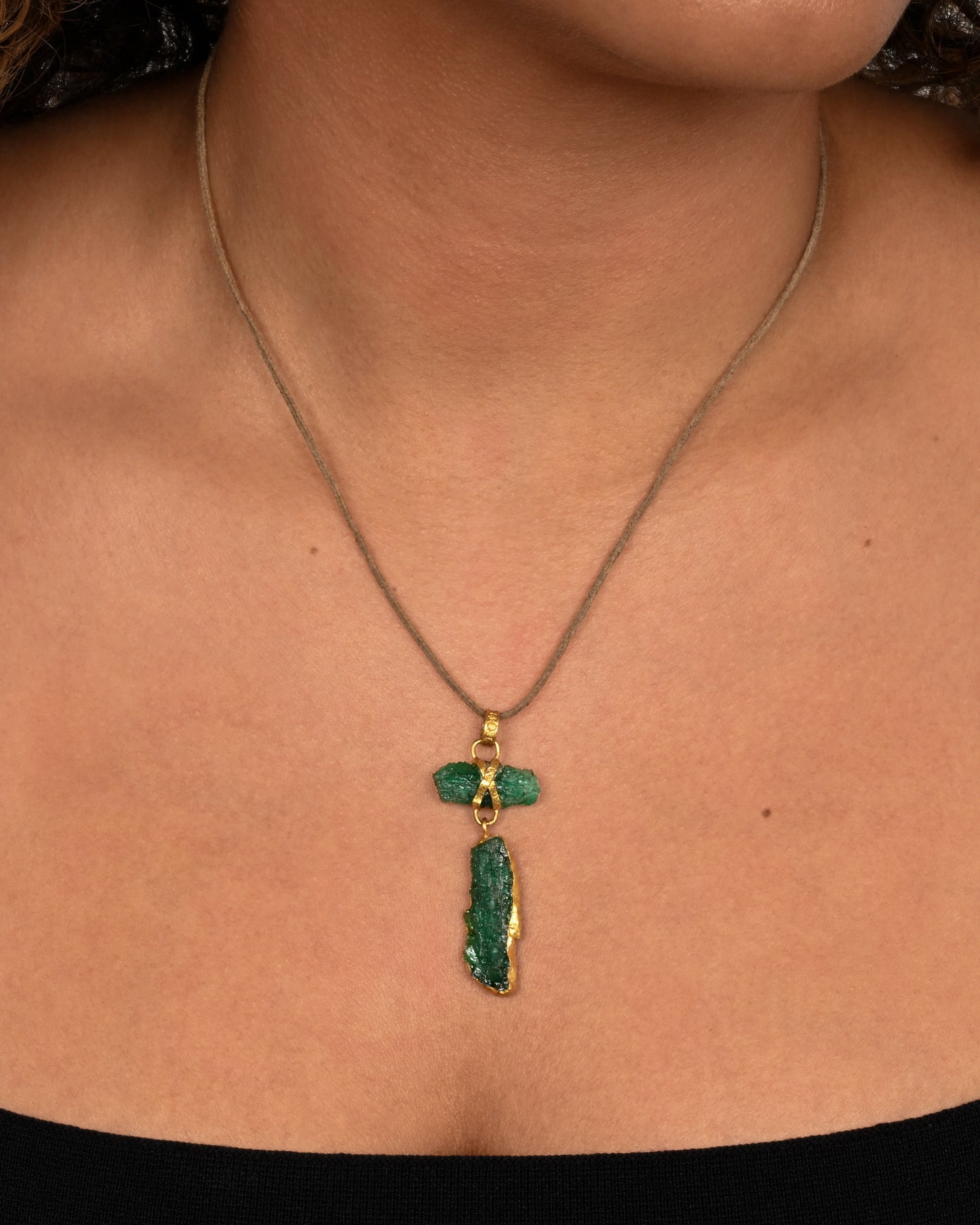 A high karat yellow gold necklace with an two raw emeralds on a cord. Shown worn around the neck.