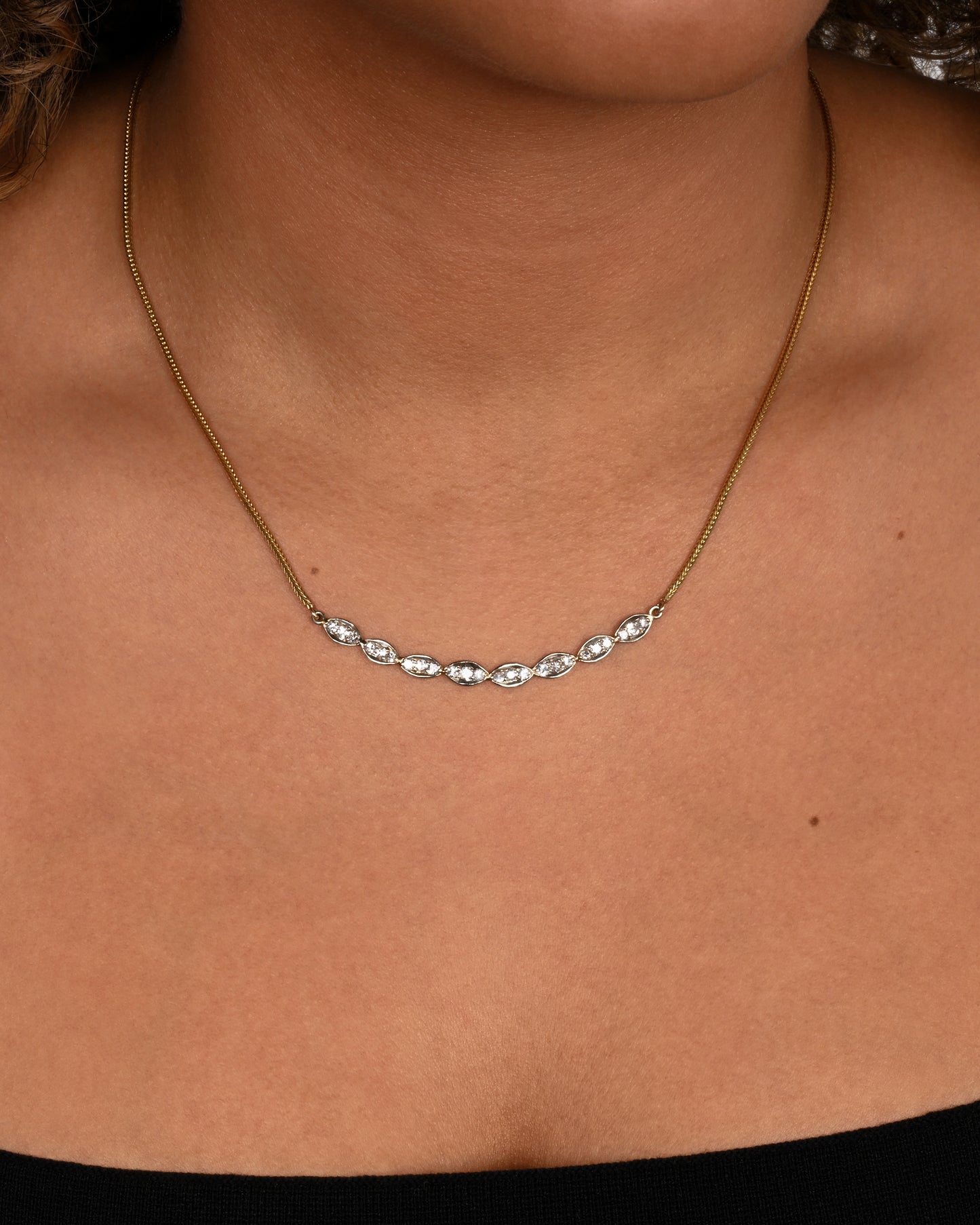 A white gold scallop edge curved bar necklace with diamonds on a yellow gold chain. Shown on a neck.