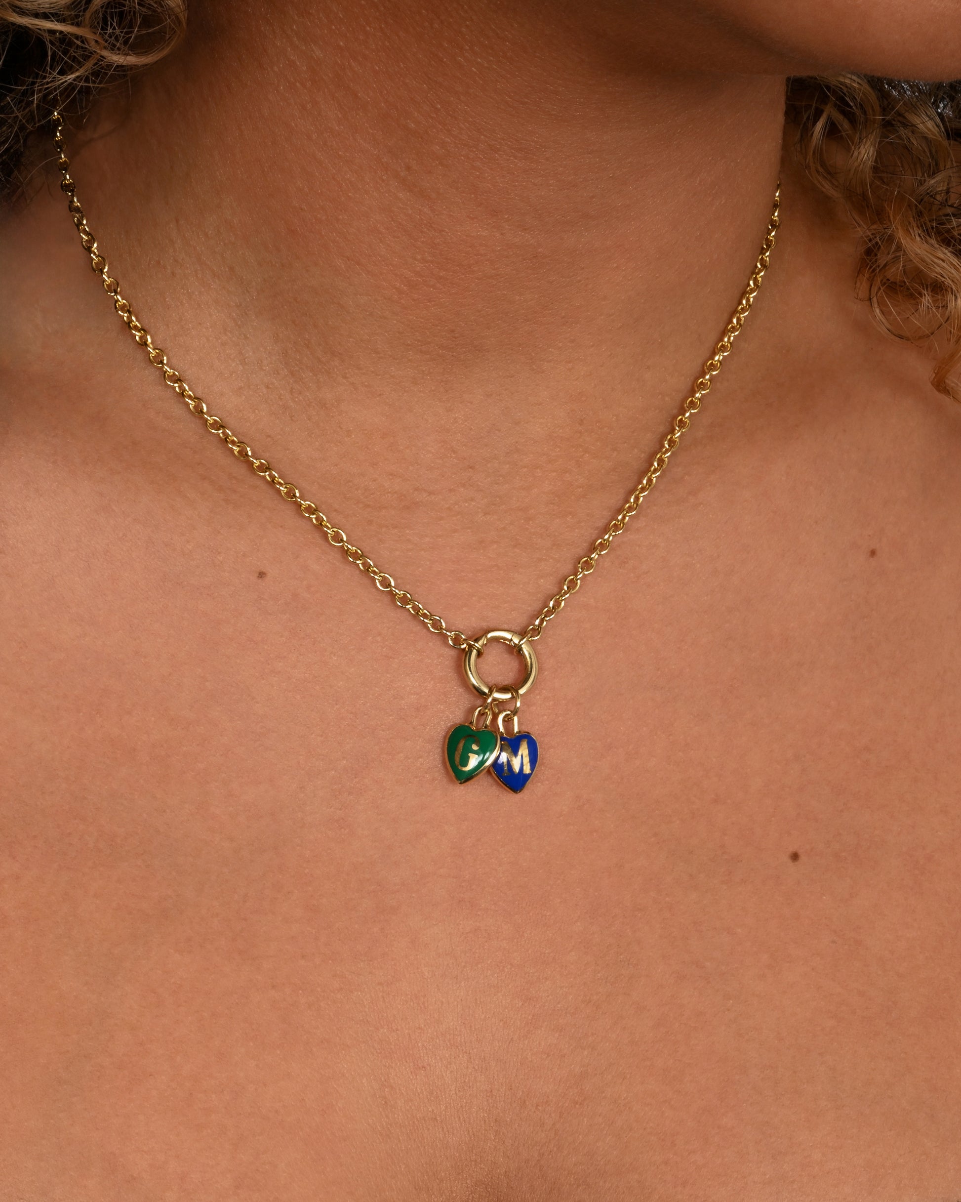 A yellow gold letter "W" heart shaped charm with red enamel. Shown worn in a different color styled with another initial charm.