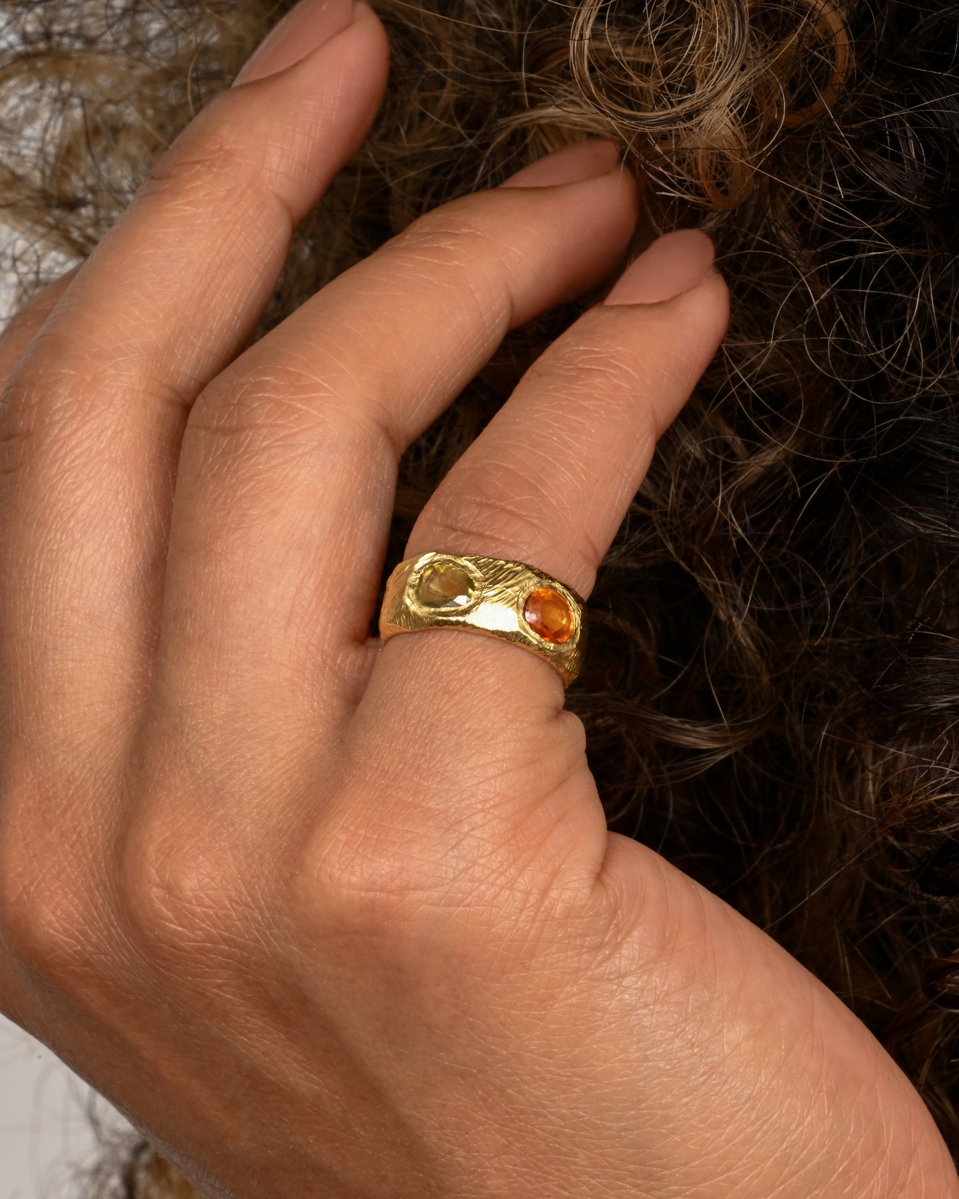 A yellow gold band with rose cut multicolor sapphires all the way around. Shown worn on a finger.