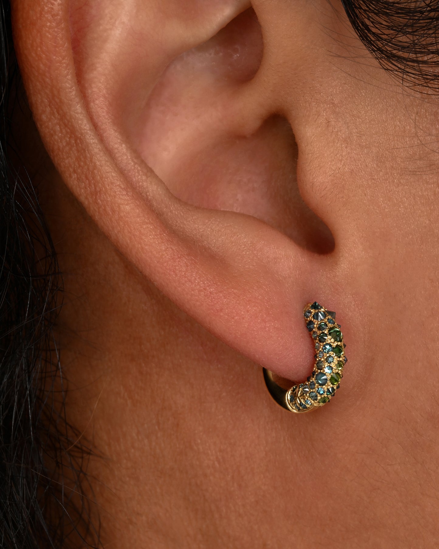 Inverted green diamonds set in yellow gold huggie hoops. Shown on an ear.