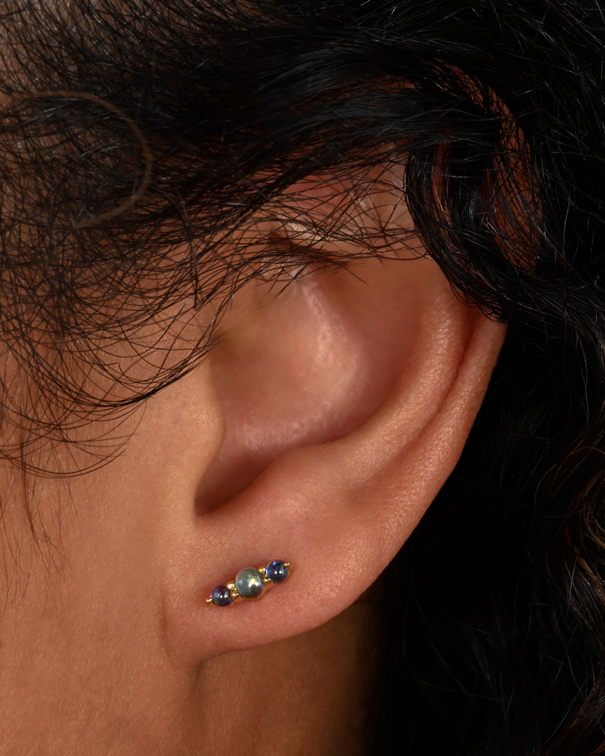 Stud earrings made of three blue sapphire cabochons set in yellow gold. Shown on an ear.