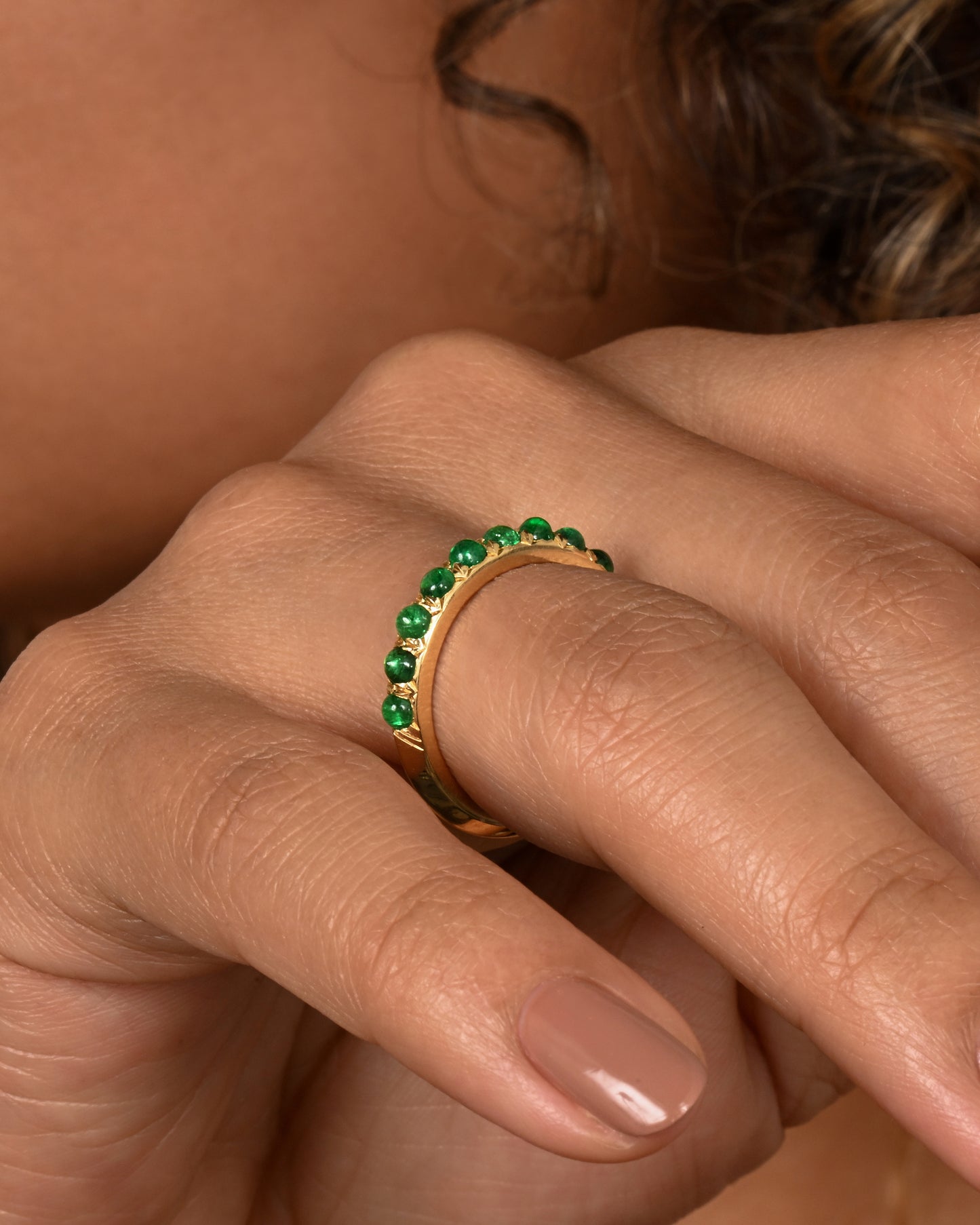 A yellow gold eternity band with emerald cabochons. Shown on a hand.