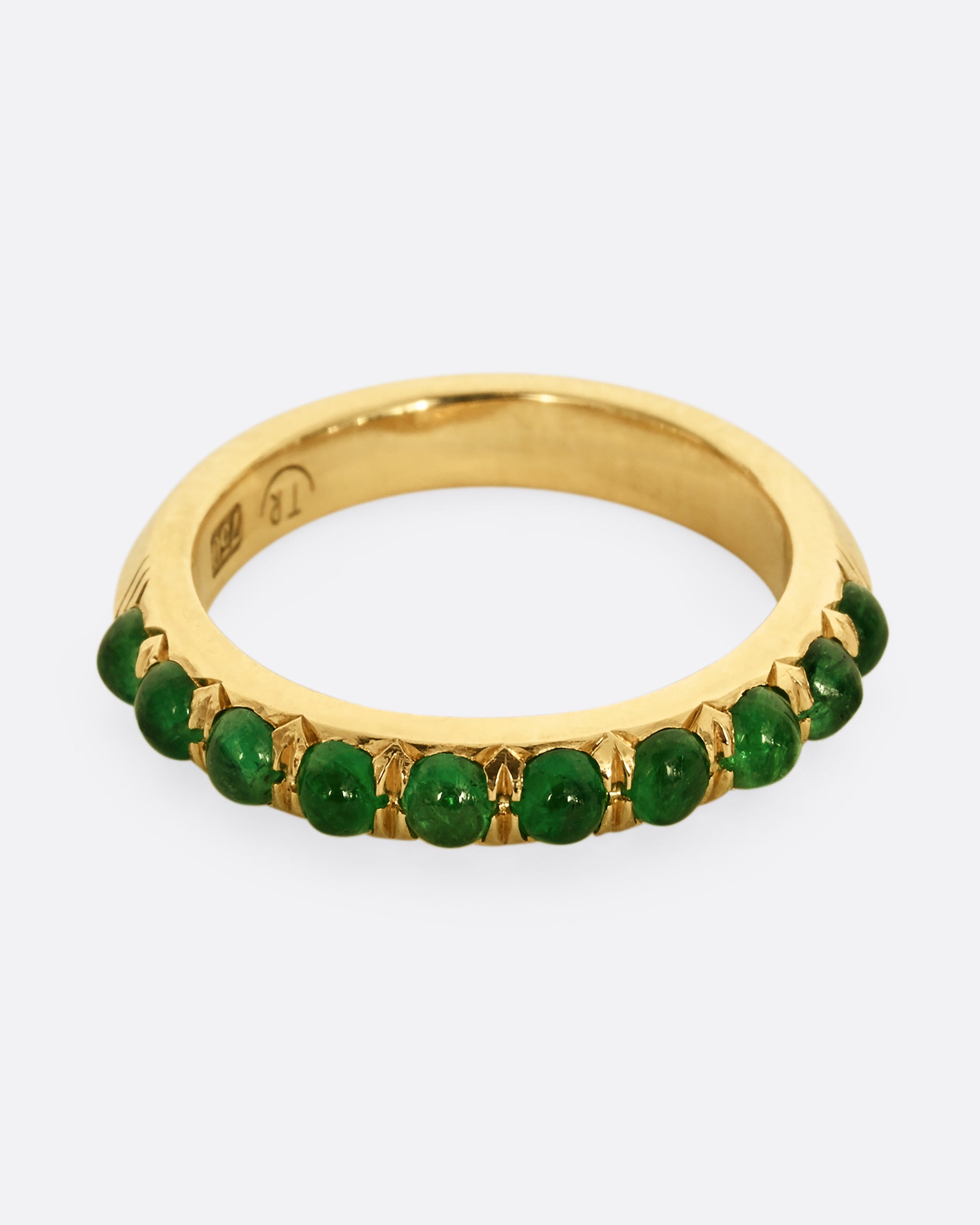 A yellow gold eternity band with emerald cabochons. Shown from the front.