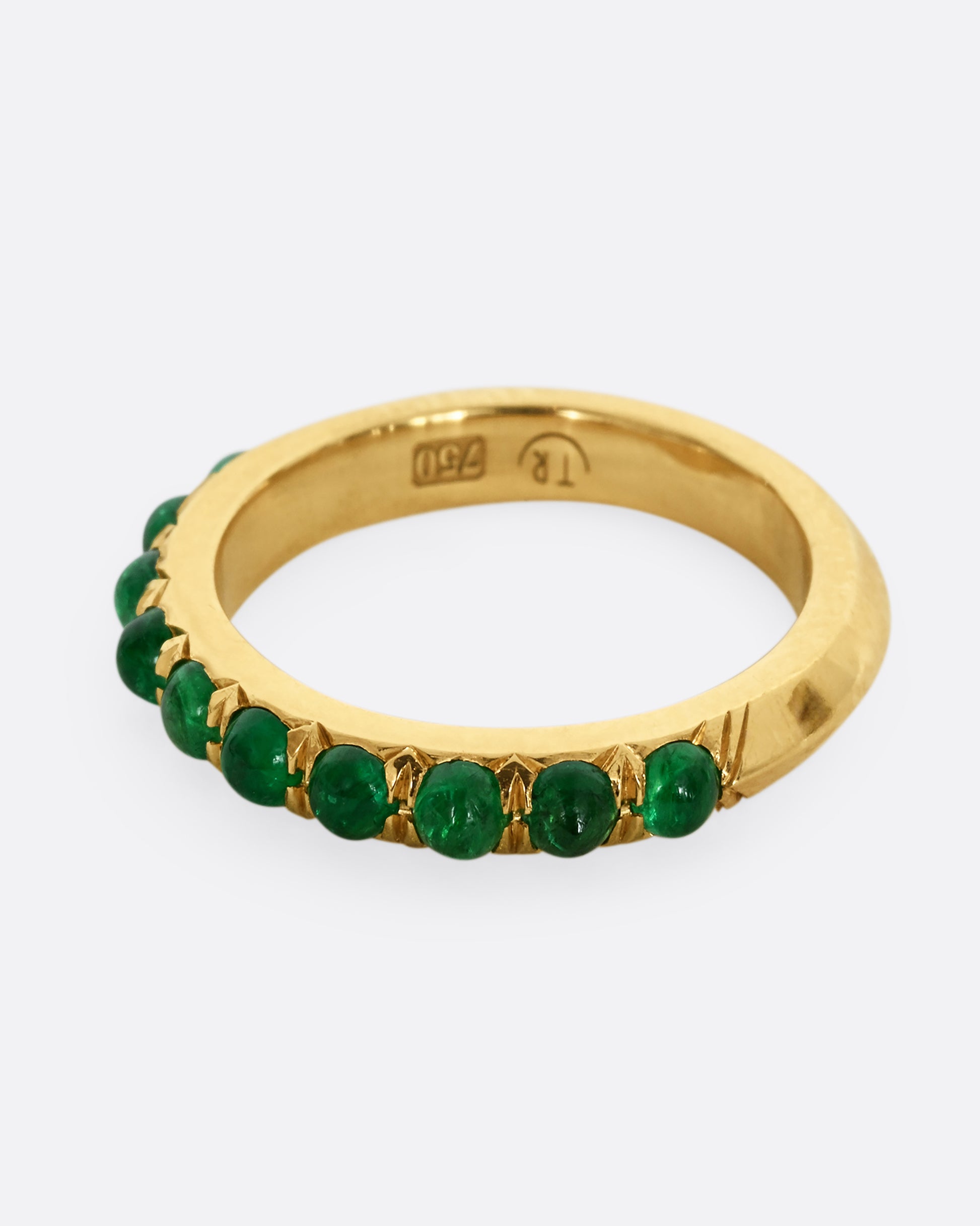 A yellow gold eternity band with emerald cabochons. Shown from the side.