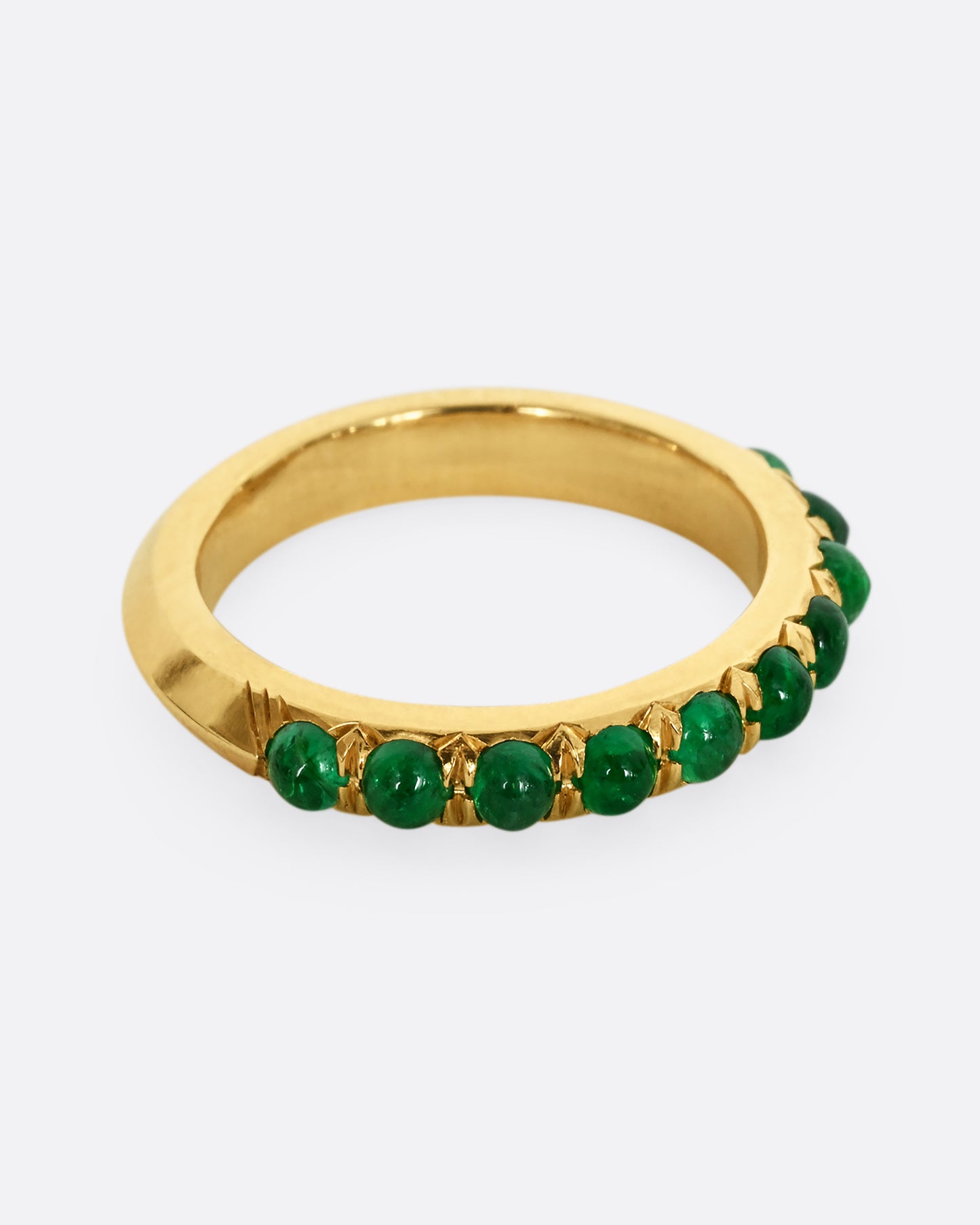 A yellow gold eternity band with emerald cabochons. Shown from the side.