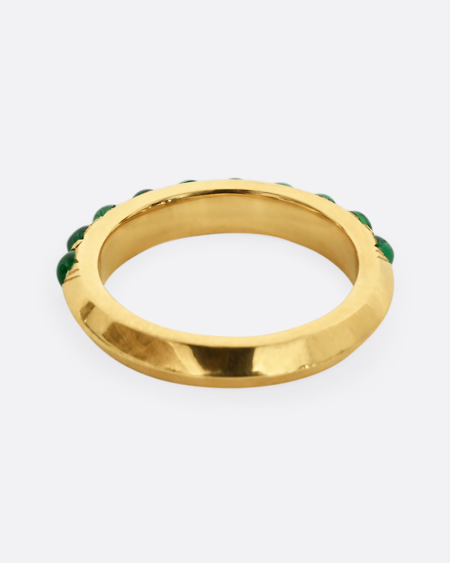 A yellow gold eternity band with emerald cabochons. Shown from the back.