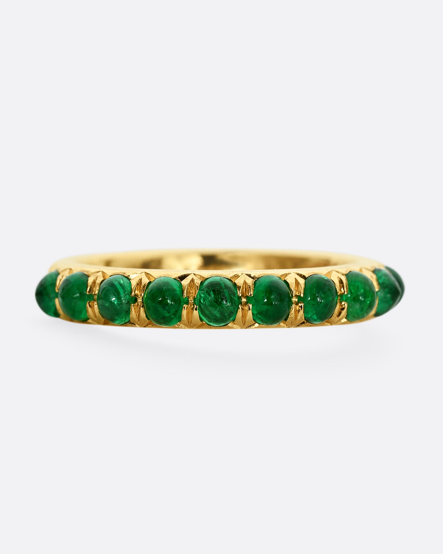 A yellow gold eternity band with emerald cabochons. Shown from the front.